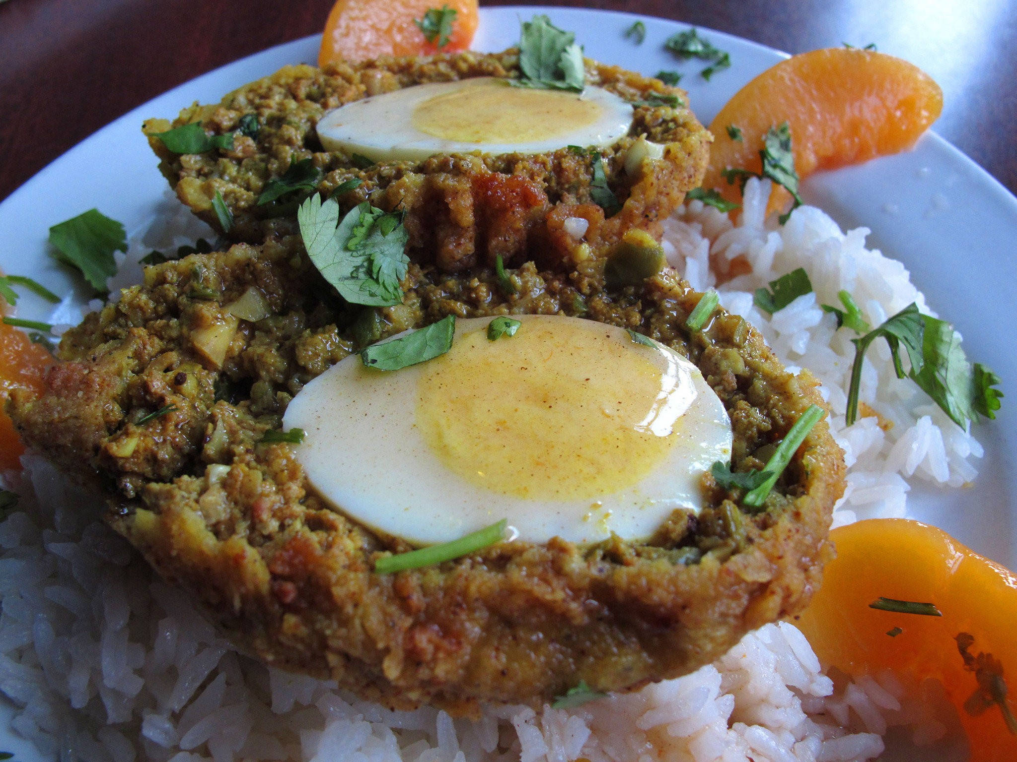 Egg 桌布 壁紙 — 兩個金棕色蘇格蘭蛋，流心蛋黃，放在白飯上，飾以香菜和柳橙片。