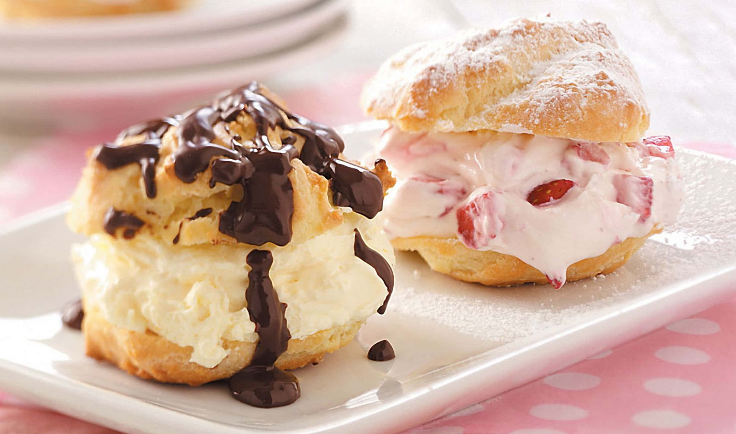 2440x1440 Desserts 桌布 壁紙 — 兩個金色泡芙，一個淋上巧克力，另一個填滿草莓奶油，撒上糖粉，放在白色盤子上。