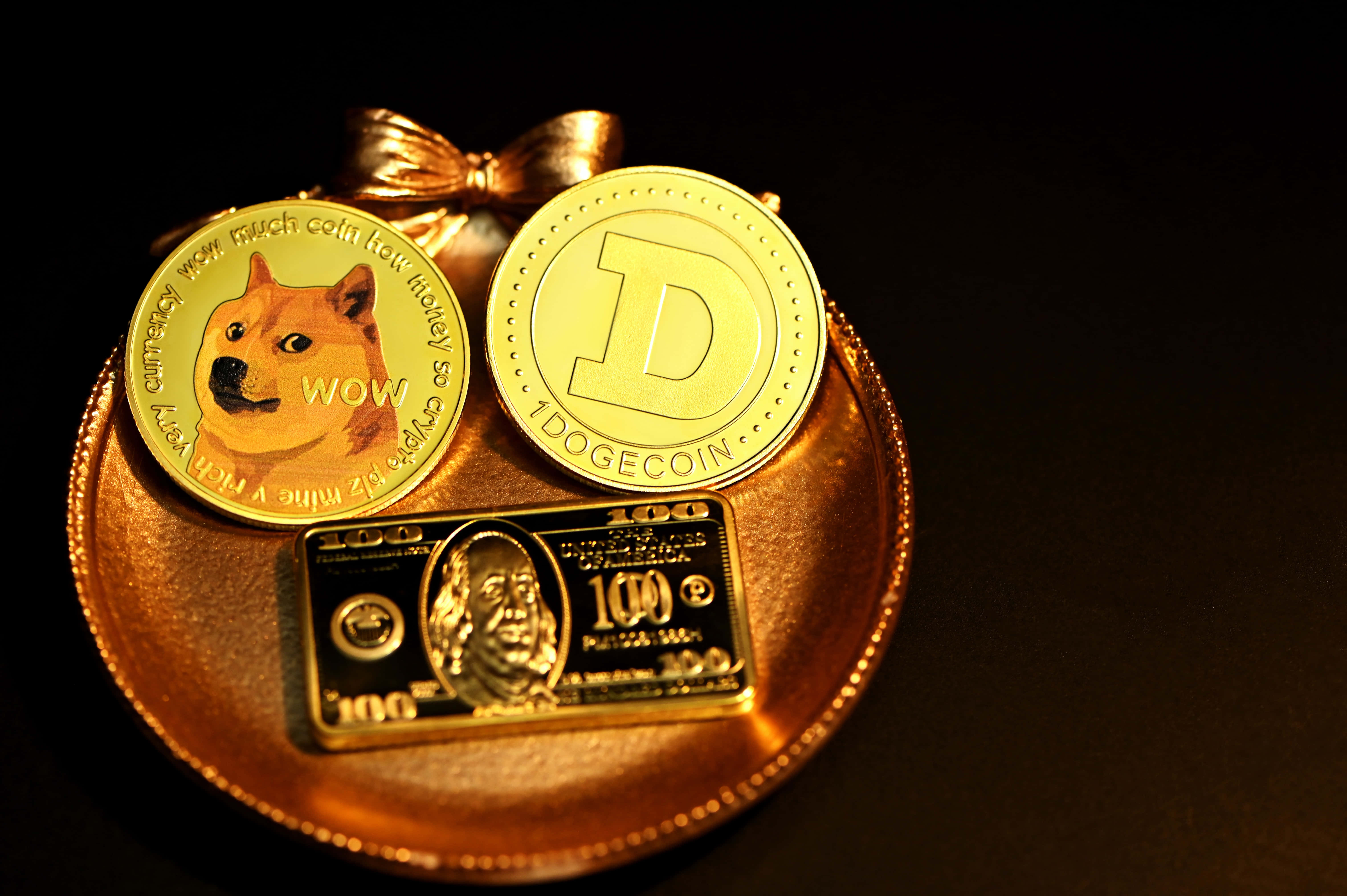 Dogecoin 桌布 壁紙 — 兩個金色狗狗幣代幣和一張鍍金100美元鈔票放在一個帶蝴蝶結的金色托盤上，背景為深色。