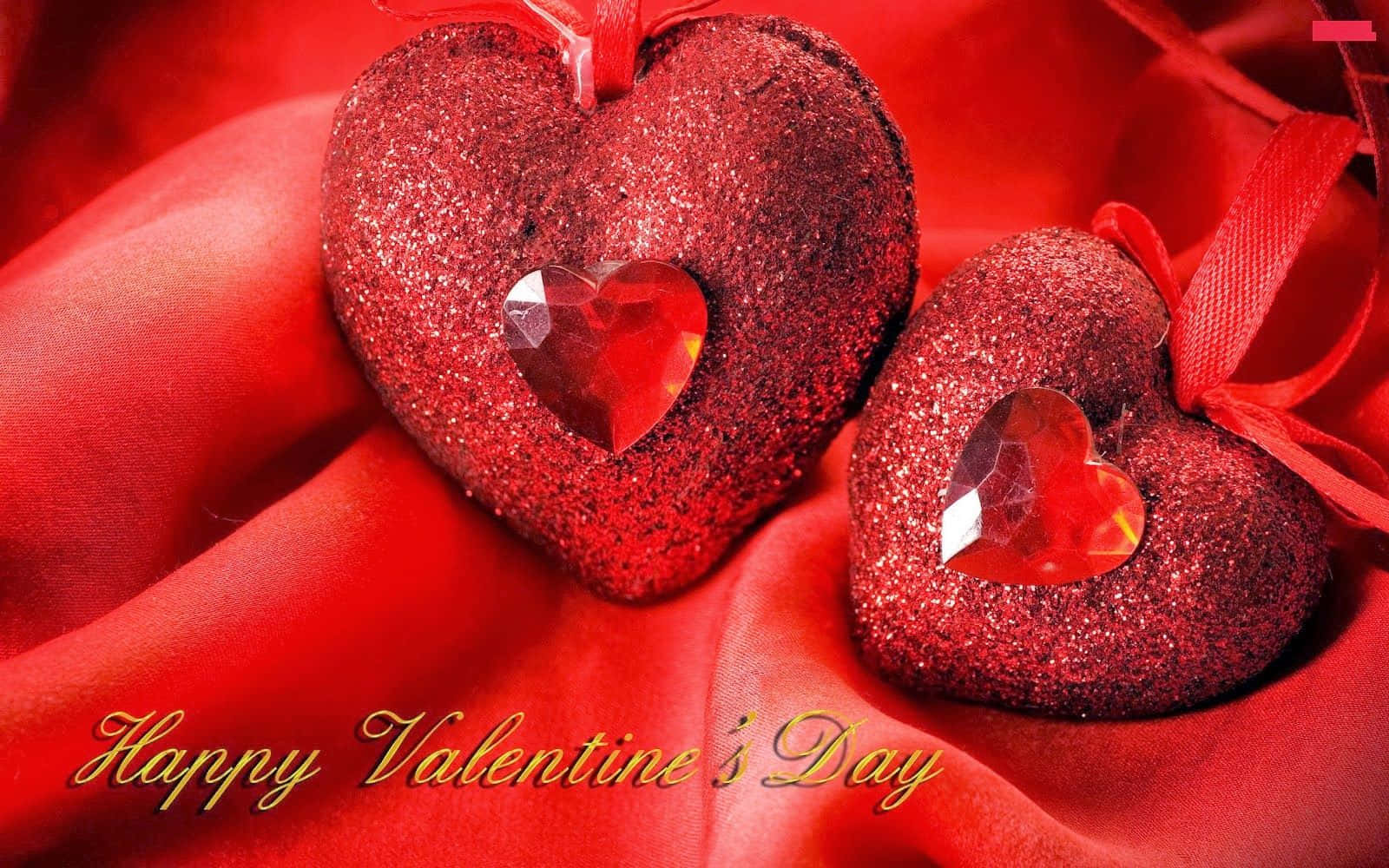 Valentines 桌布 壁紙 — 兩個閃亮紅色心形裝飾品，內有水晶心形，放置在豐富的紅色緞面布料上，並有情人節文字。