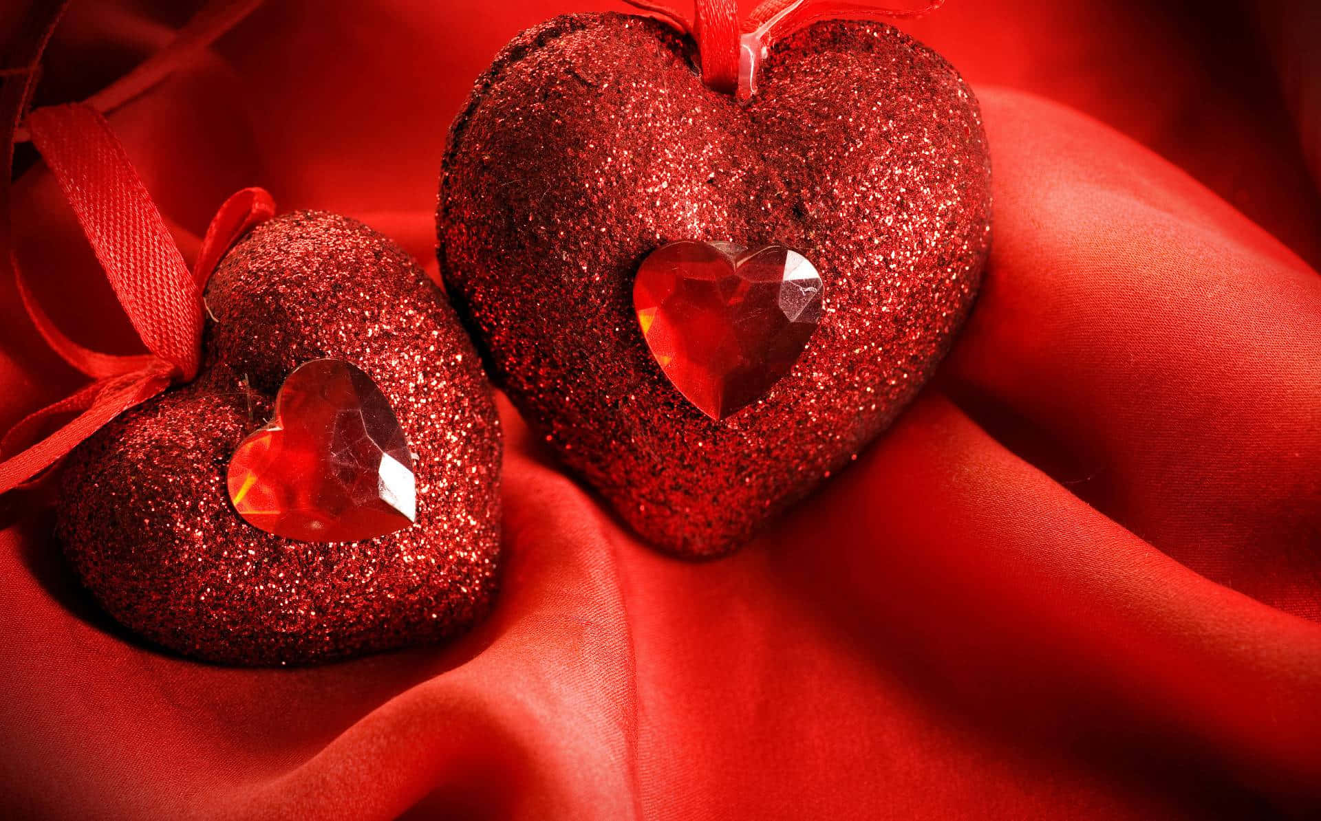 3d Heart 桌布 壁紙 — 兩個閃閃發光的紅色心形裝飾品，裡面有水晶心，放在柔軟的紅色布料上。