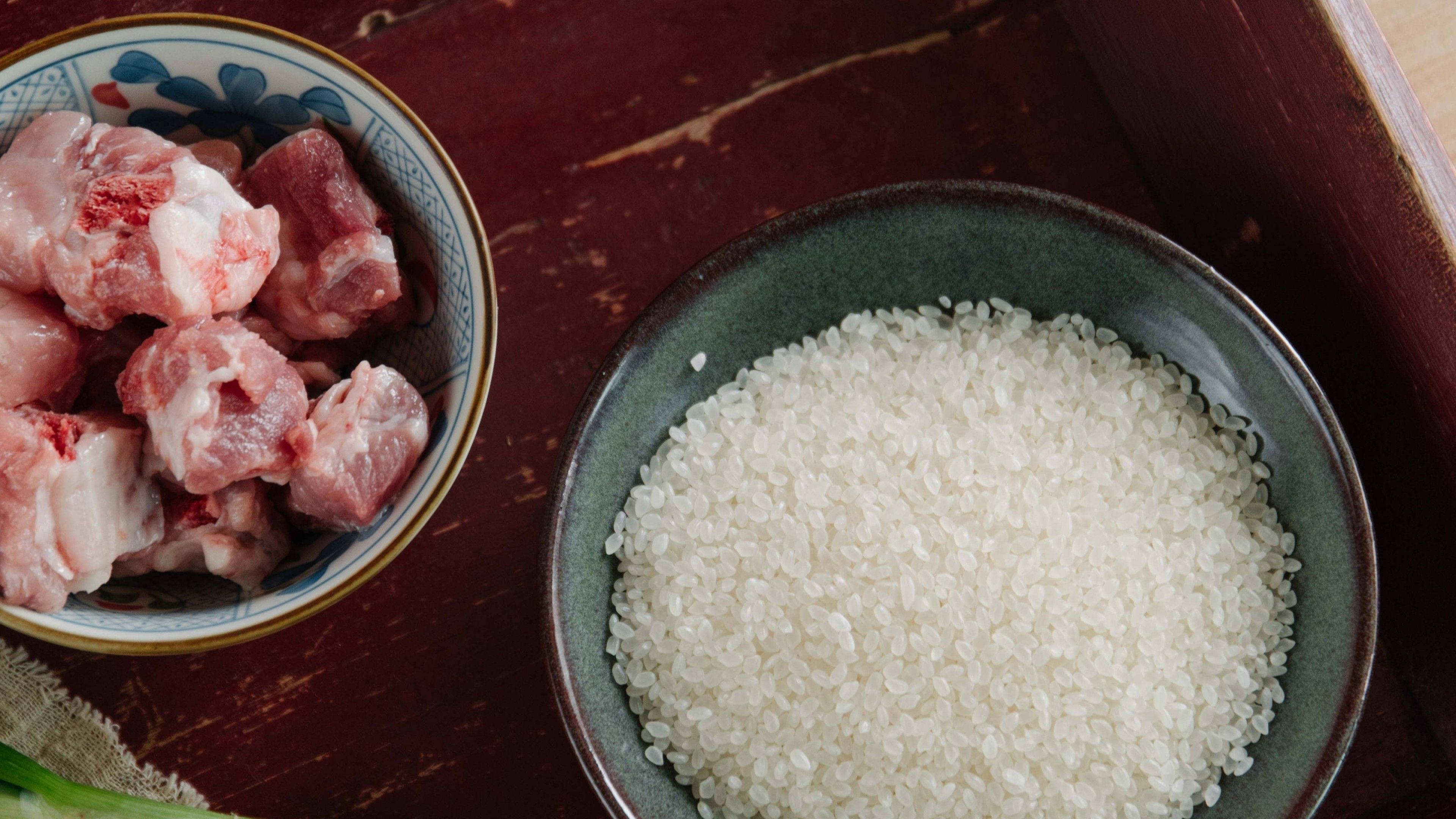 烹飪 桌布 壁紙 — 兩個陶瓷碗盛載生豬肉塊和白飯，放在深色木質表面上。