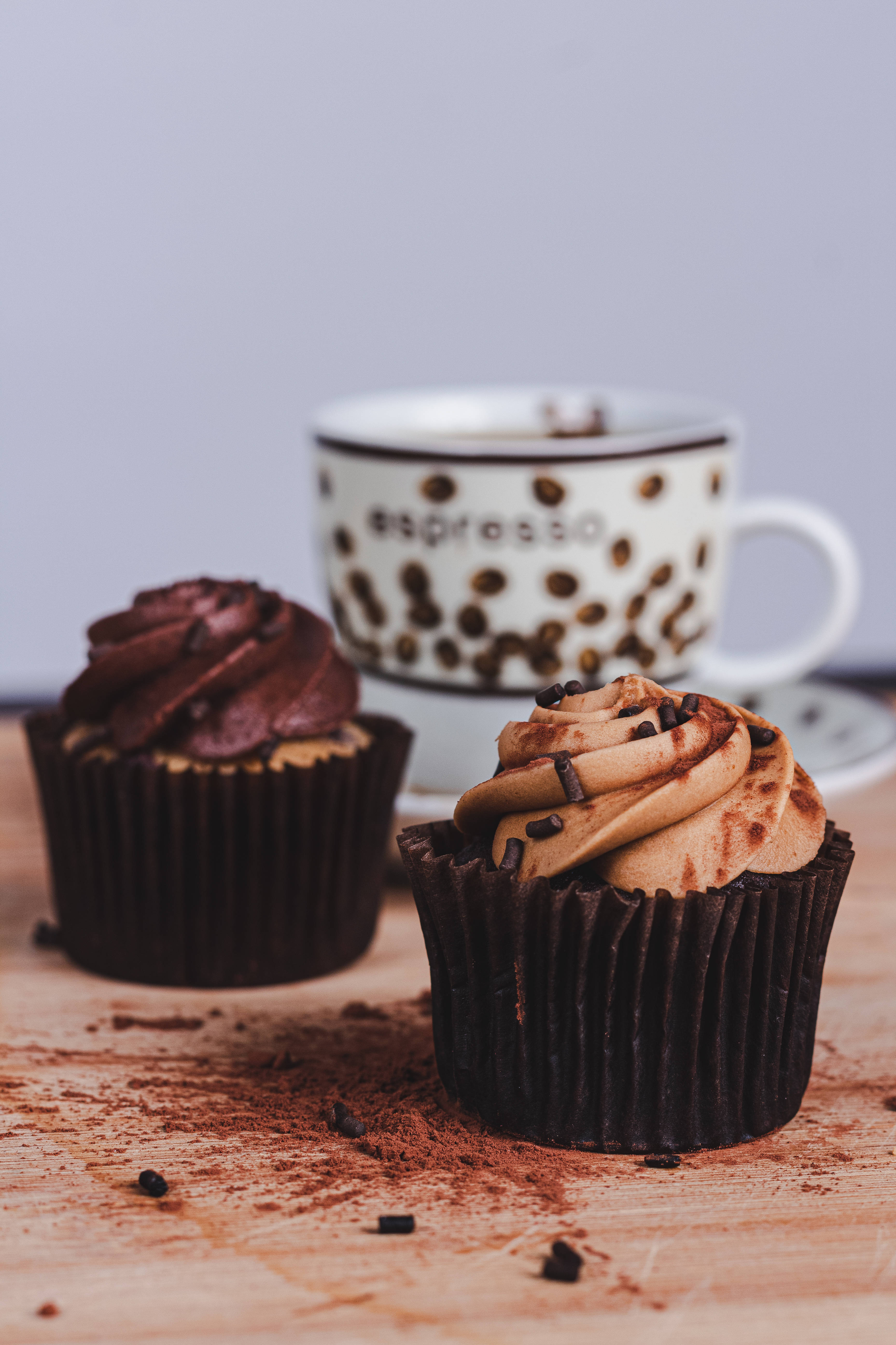 Cupcake 桌布 壁紙 — 兩個頹廢的巧克力紙杯蛋糕，上面有糖霜和可可粉的漩渦，旁邊放著一杯咖啡在木質表面上。