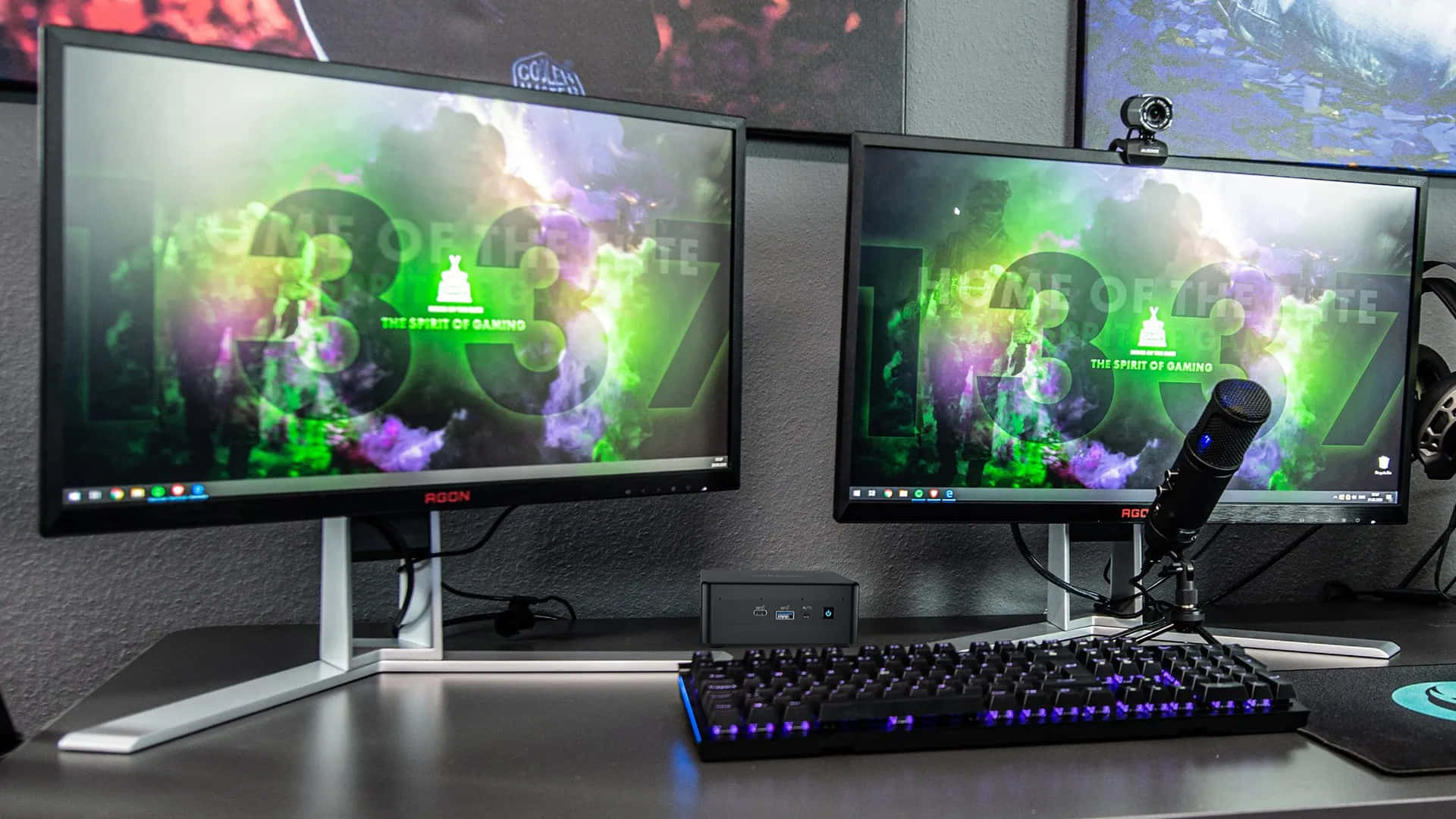 Gaming Pc 桌布 壁紙 — 兩個顯示器顯示充滿活力的綠色和紫色遊戲壁紙，位於發光的鍵盤和麥克風上方，放在時尚的桌子上。