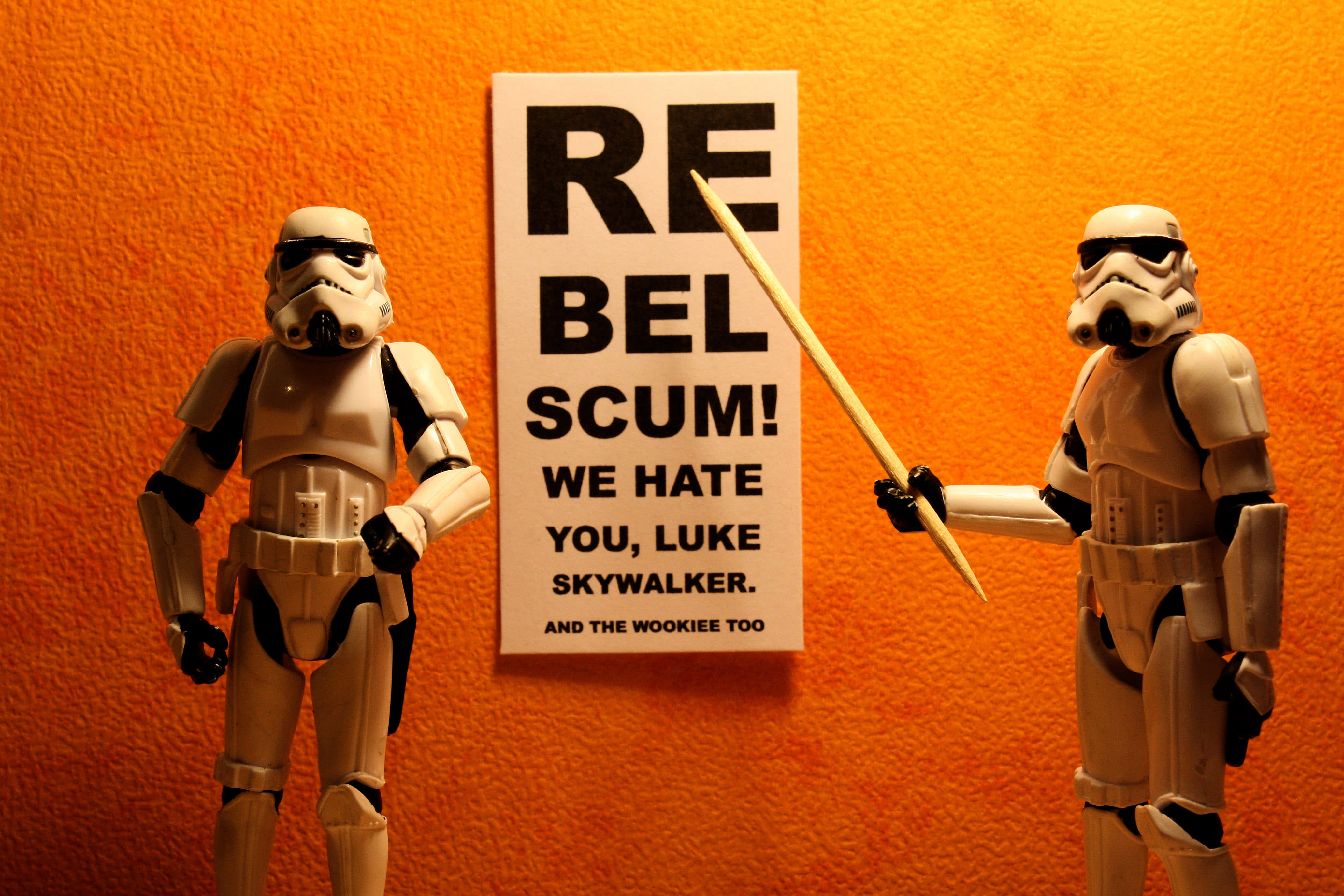 Funny Star Wars 桌布 壁紙 — 兩個風暴兵人偶站在一個橙色牆壁前，對路克·天行者及烏奇族表達憎恨的標語牌前。