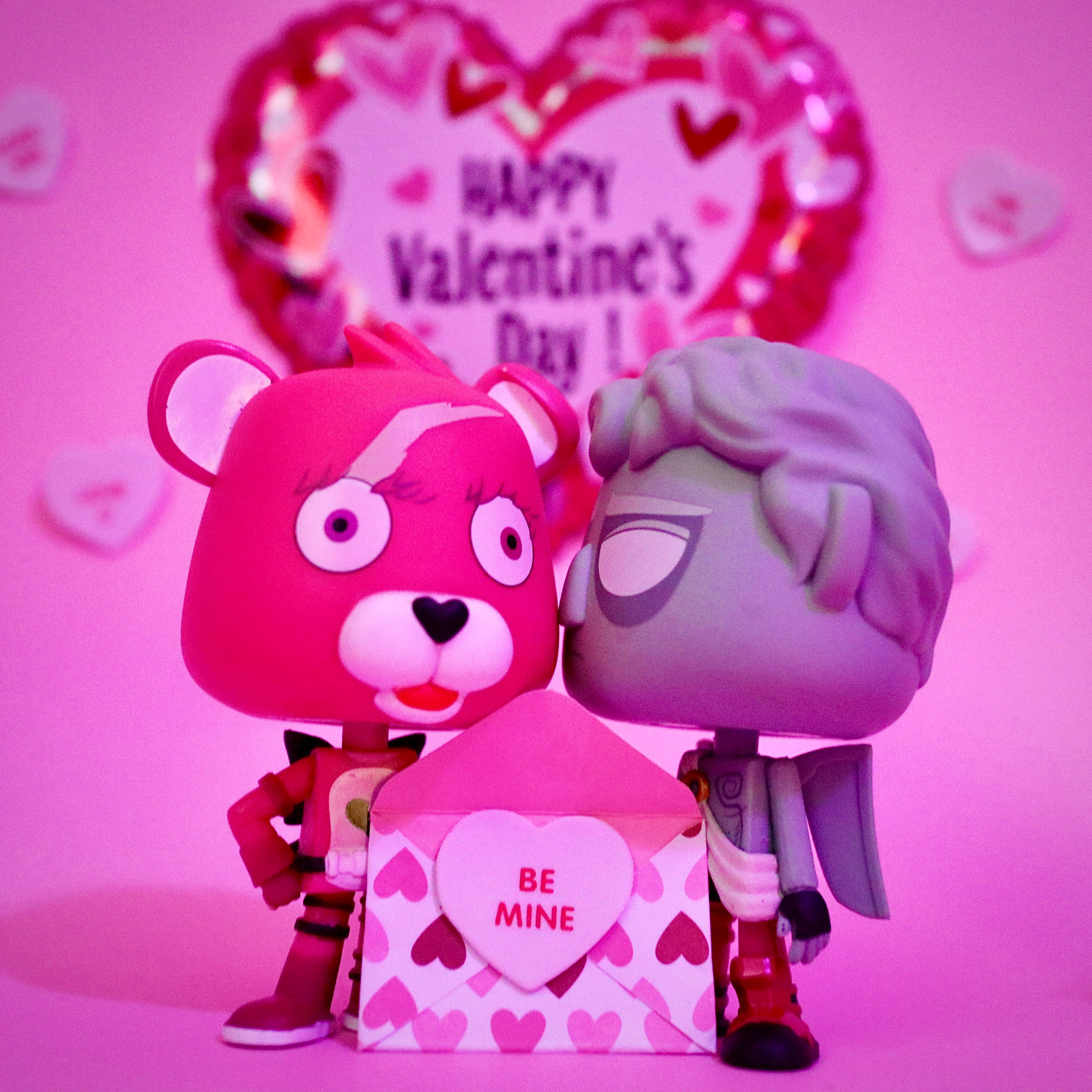 Funko Pop 桌布 壁紙 — 兩個風格化公仔在粉紅色心形氣球背景下擁抱一個心形情人節禮物盒。