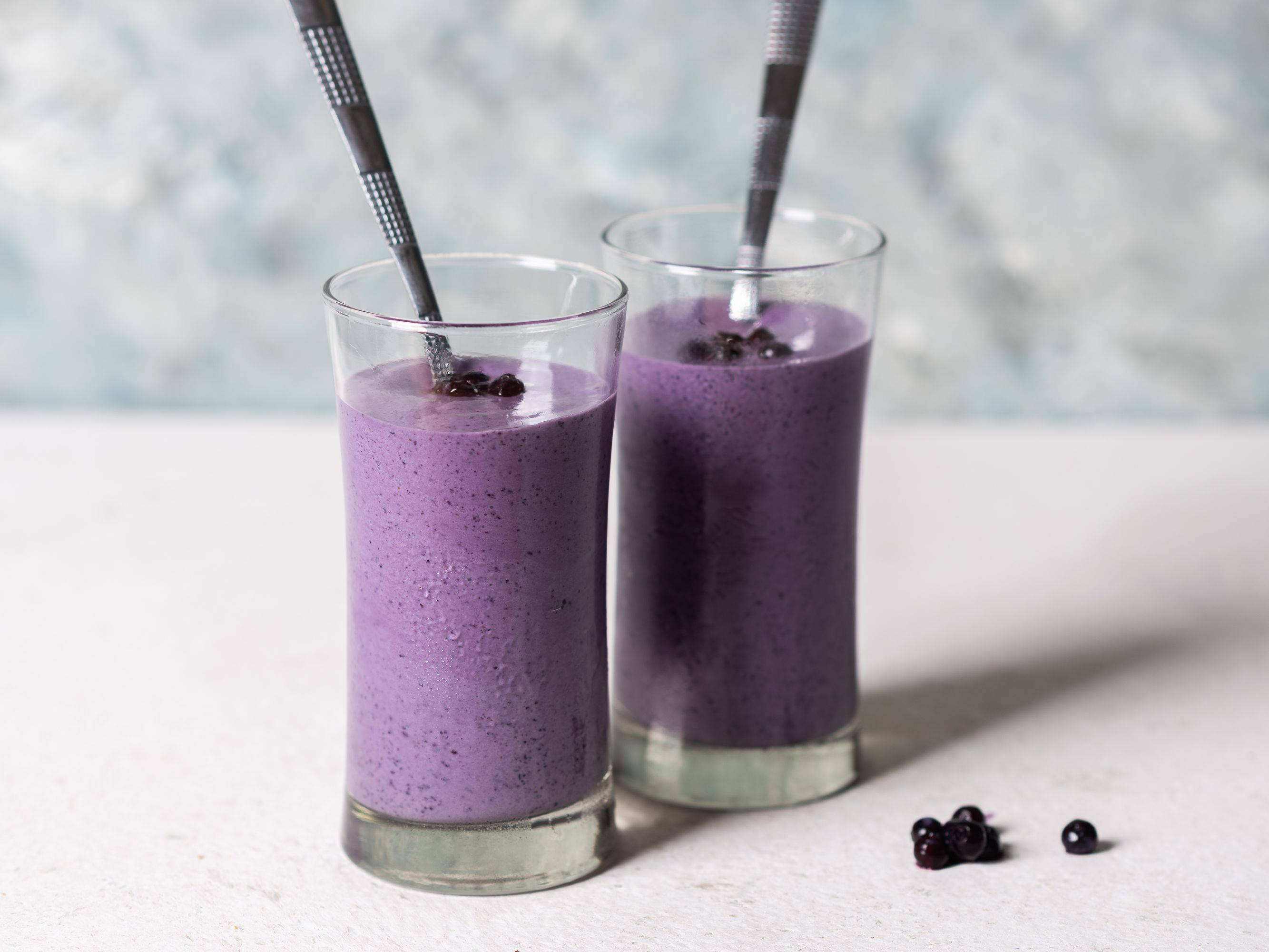 Smoothie 桌布 壁紙 — 兩個高身玻璃杯裝滿充滿活力的紫色冰沙，上面放有黑莓並撒上種子，放在帶有紋理灰色背景的白色表面上。
