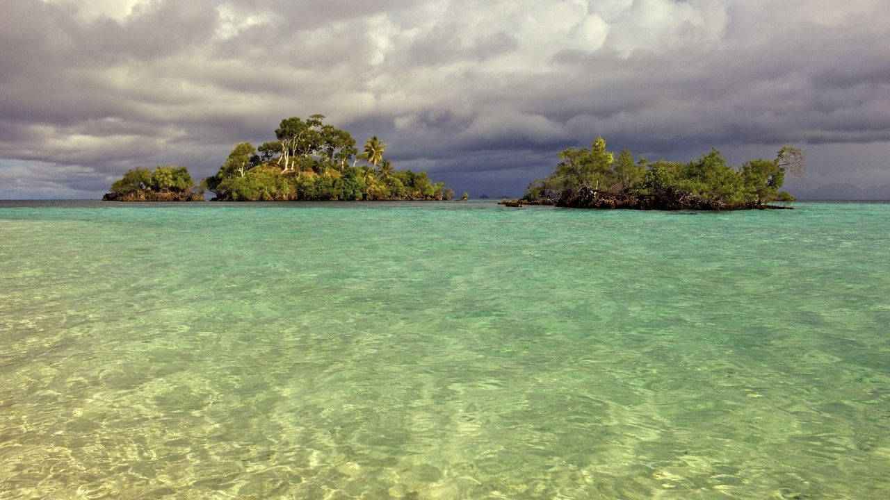 Palau 桌布 壁紙 — 兩個鬱鬱蔥蔥的綠色熱帶島嶼從清澈的碧綠海水中升起，天空多雲而戲劇化。