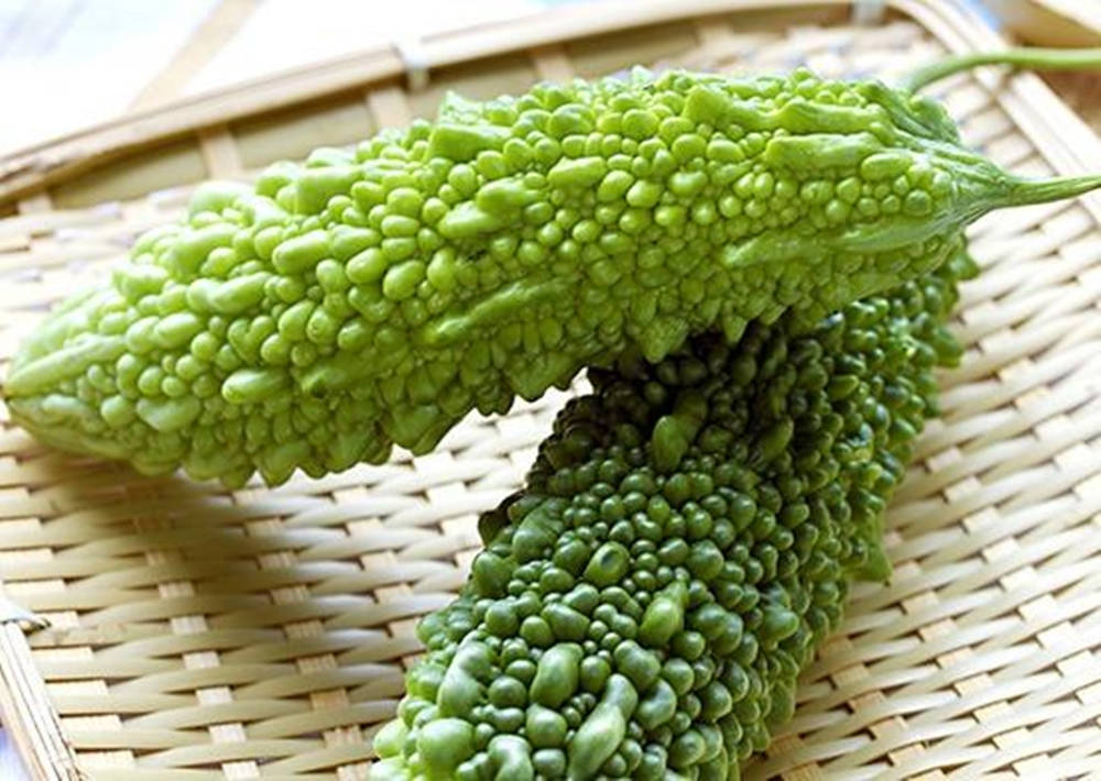 Food Photography 桌布 壁紙 — 兩個鮮綠色的苦瓜，表面凹凸不平，在明亮燈光下放在編織竹蓆上。