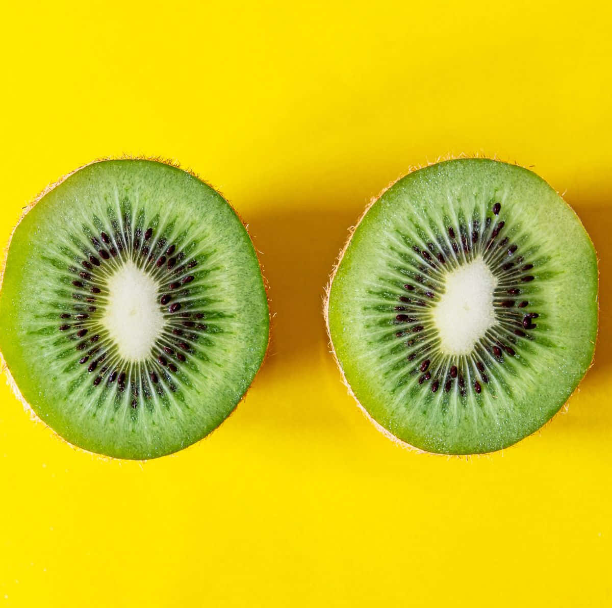 Fruit 桌布 壁紙 — 兩個鮮豔的奇異果半邊在鮮黃色背景上展現多汁的綠色果肉和黑色種子。