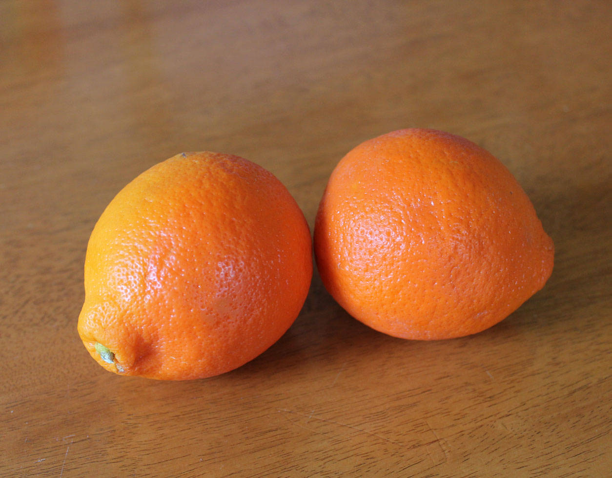 Fruits 桌布 壁紙 — 兩個鮮豔的柳橙並排放在溫暖的木質表面上，光線柔和自然。
