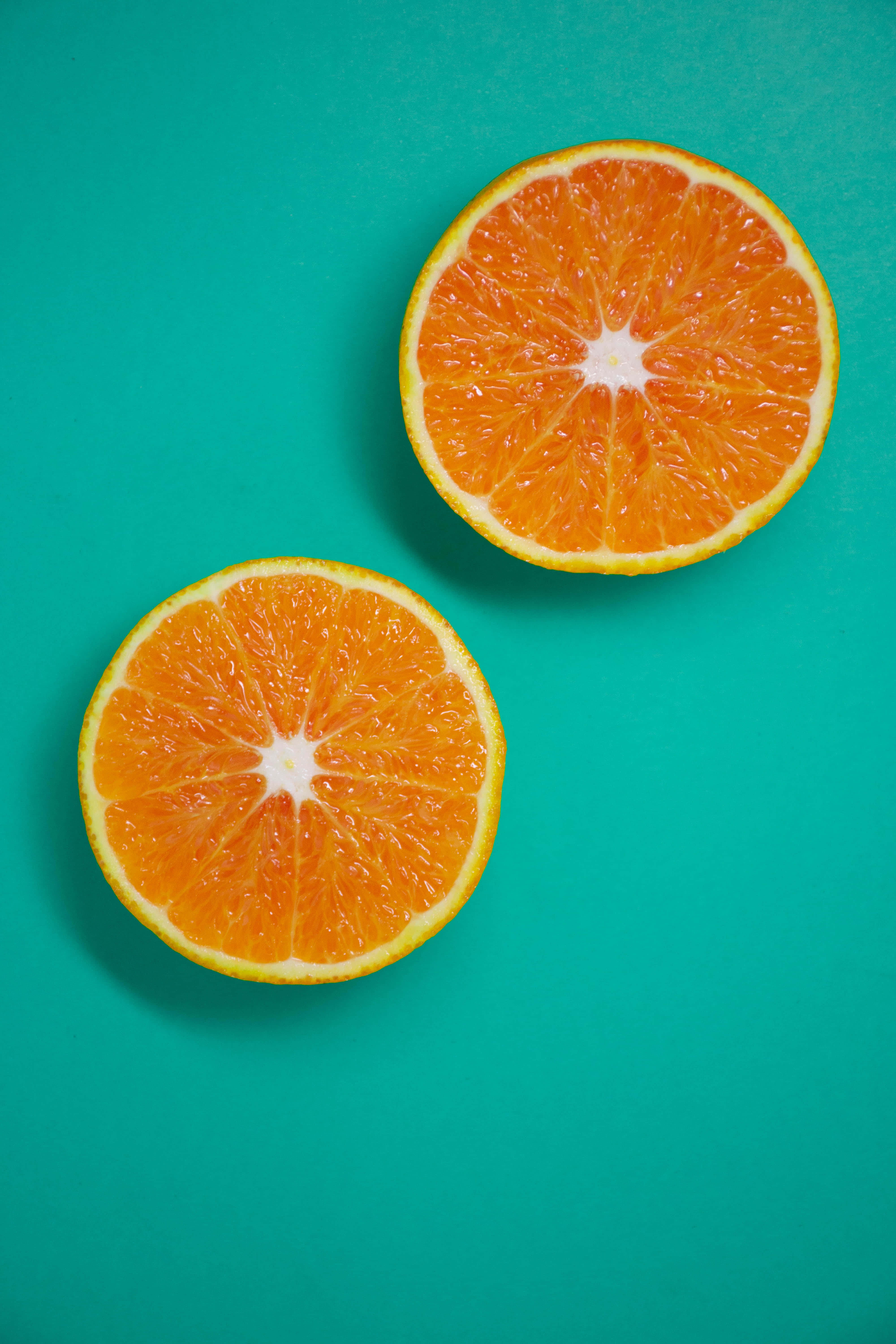 Orange Slice 桌布 壁紙 — 兩個鮮豔的橙半邊放在青綠色背景上，展示多汁的果肉和明亮的果皮。