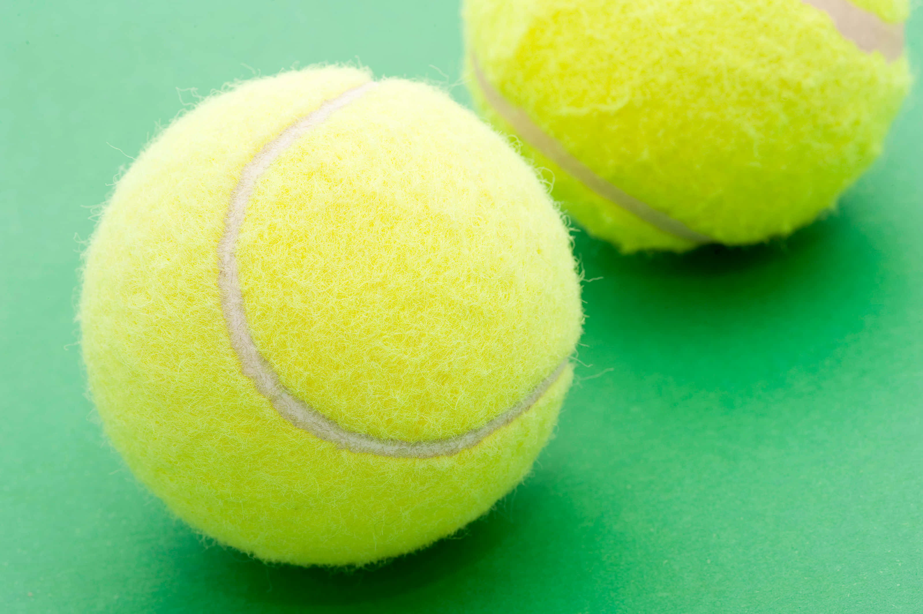 Tennis Ball 桌布 壁紙 — 兩個鮮黃色、帶絨毛質感的網球放在充滿活力的綠色表面上。