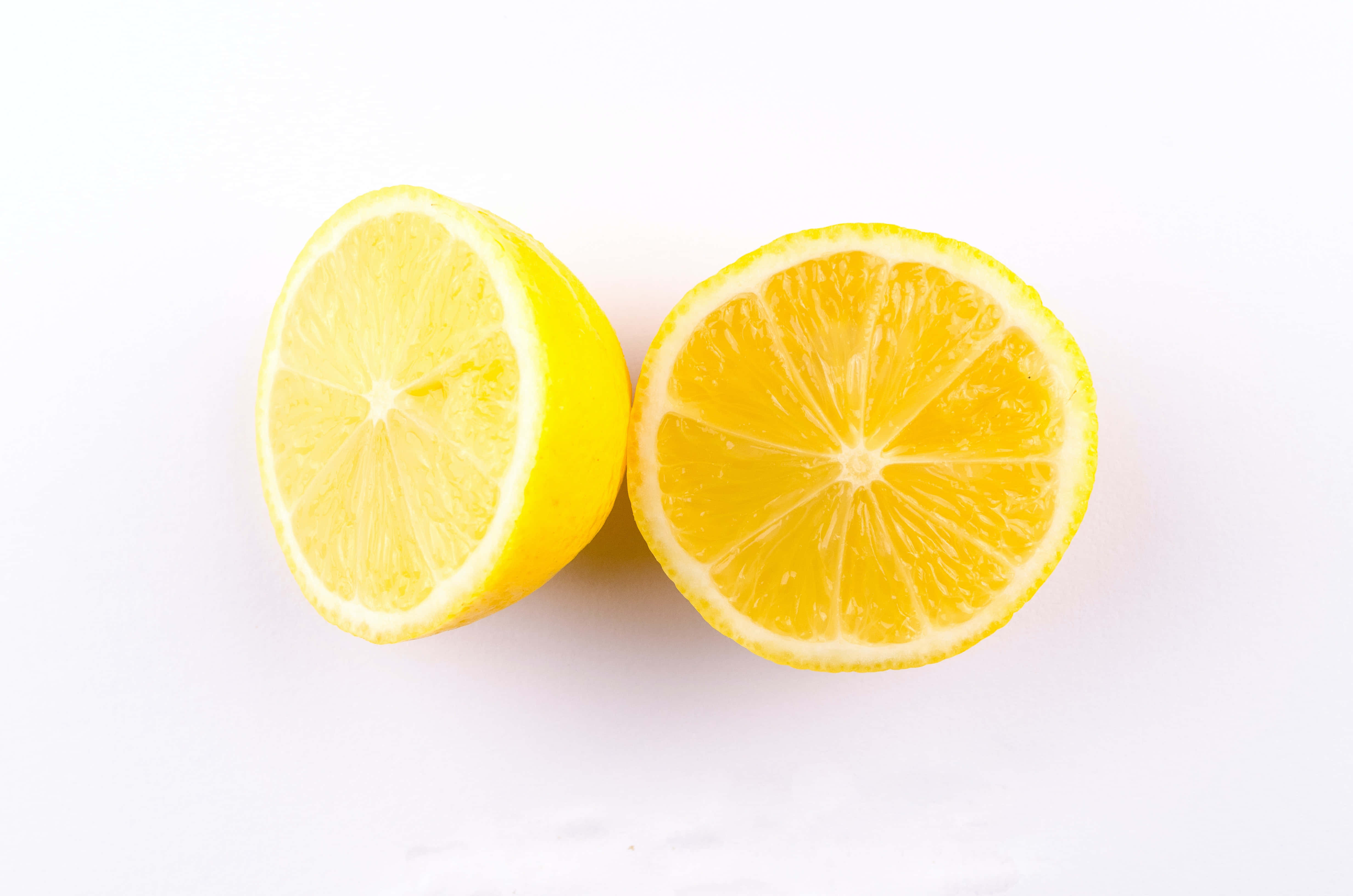 Summer Fruits 桌布 壁紙 — 兩個鮮黃色的檸檬半塊整齊地切開，放在純白色背景上，露出多汁的分瓣果肉。