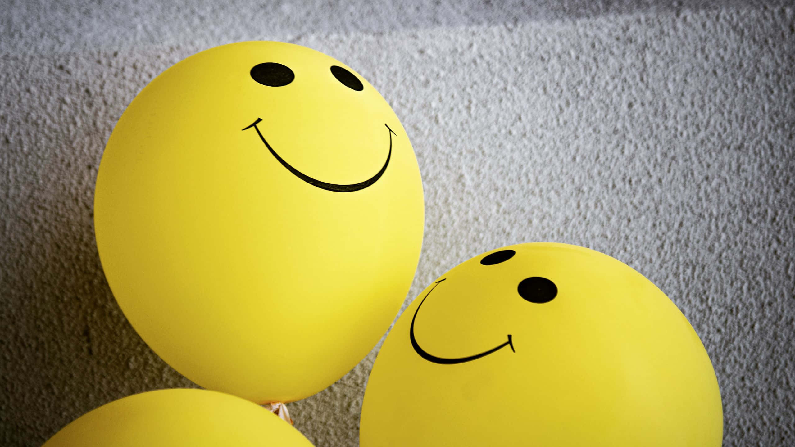 Balloons 桌布 壁紙 — 兩個鮮黃色笑臉氣球放在有紋理的灰色地毯上，光線柔和。