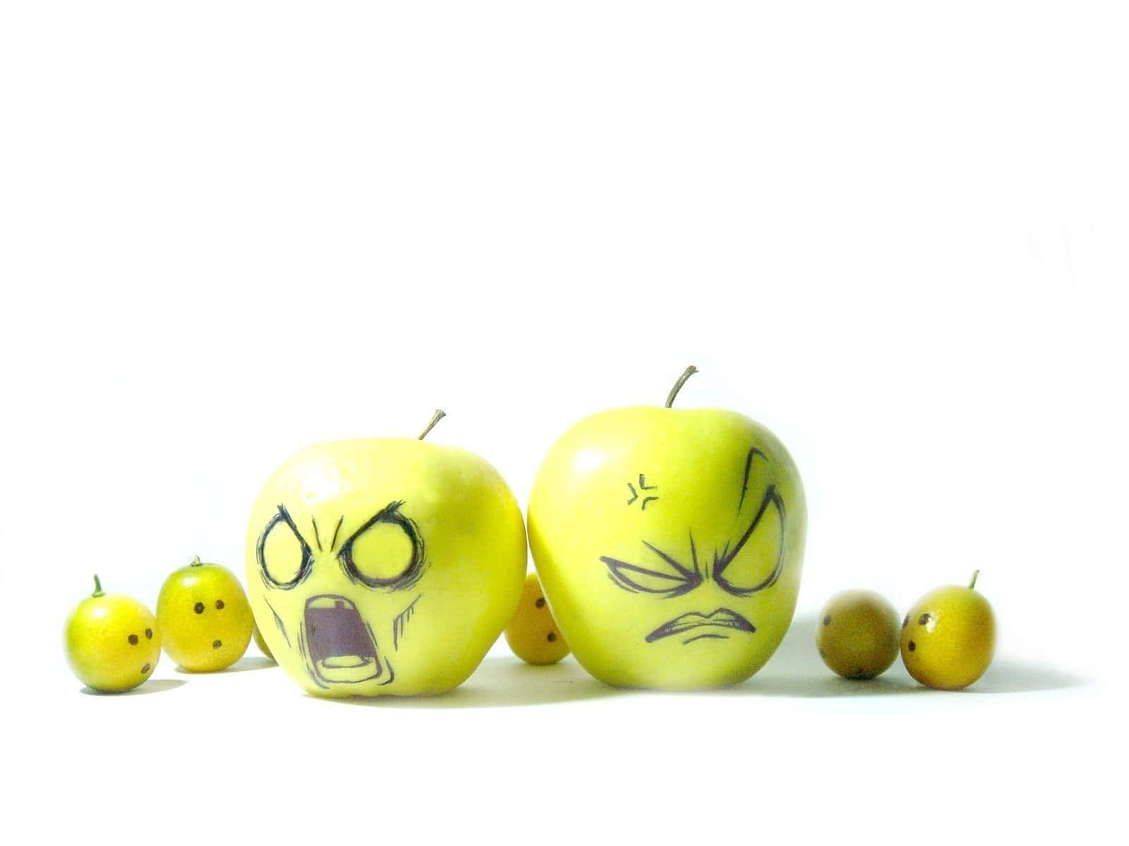Food Desktop 桌布 壁紙 — 兩個黃色蘋果上畫有憤怒的卡通臉孔，放在較小的水果之間，背景為純白色。
