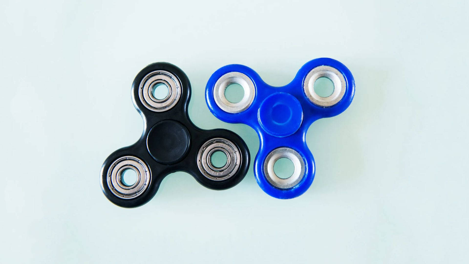 toys 桌布 壁紙 — 兩個黑色和藍色的指尖陀螺並排放在淡色背景上。