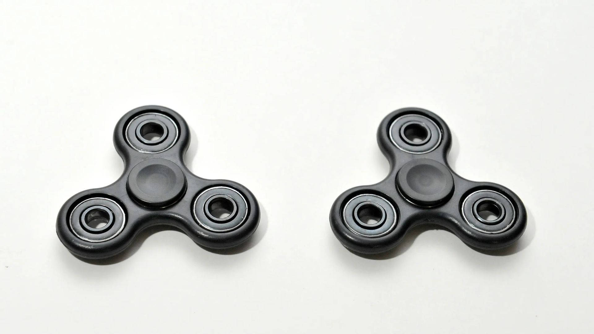 toys 桌布 壁紙 — 兩個黑色指尖陀螺並排放在乾淨的白色表面上，投下柔和的陰影。