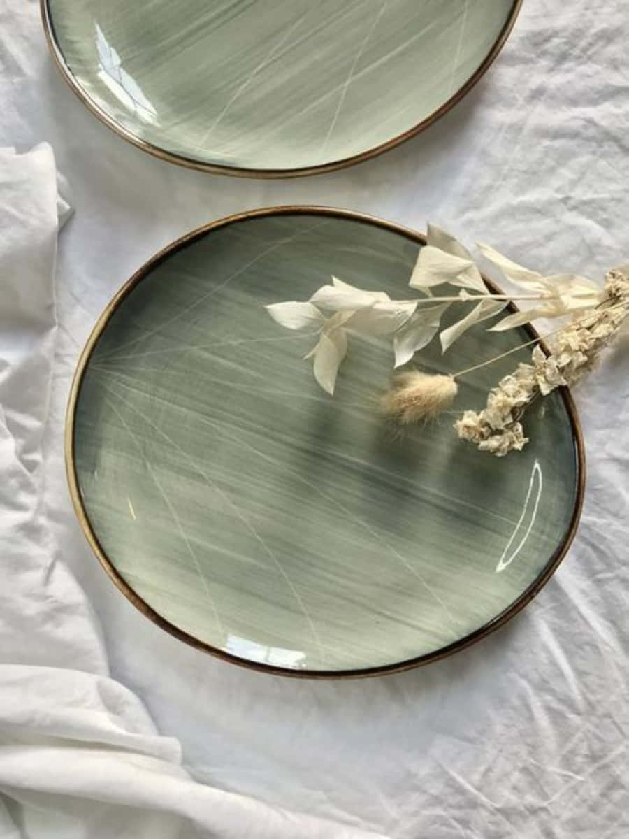 Aesthetic Sage Green 桌布 壁紙 — 兩個鼠尾草綠色陶瓷盤帶金邊，放在白色亞麻布上，飾以精緻乾燥花。