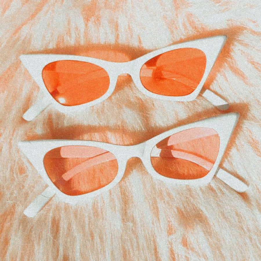 Sunglasses 桌布 壁紙 — 兩副白色貓眼太陽眼鏡搭配橙色鏡片，放置在毛絨絨的蜜桃色和奶油色紋理表面上。