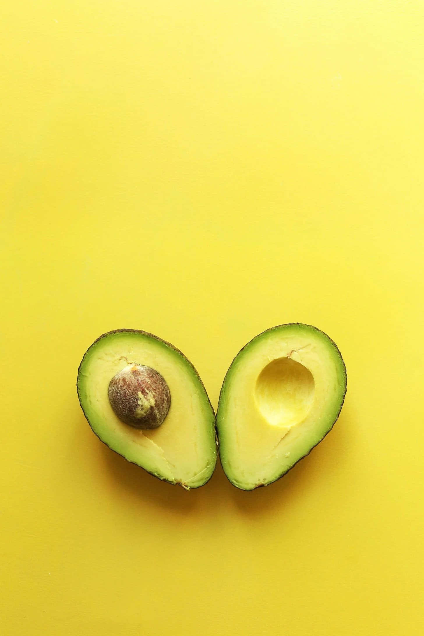 Avocado 桌布 壁紙 — 兩半成熟的酪梨連核放在鮮黃色背景上。