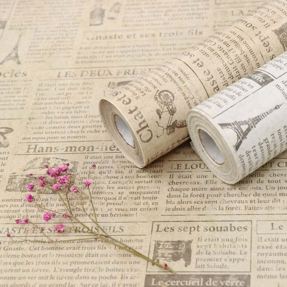 Newspaper 桌布 壁紙 — 兩卷帶有法文文字和插圖的復古報紙壁紙卷，放在相配的平板上，並以粉紅色乾花枝點綴。