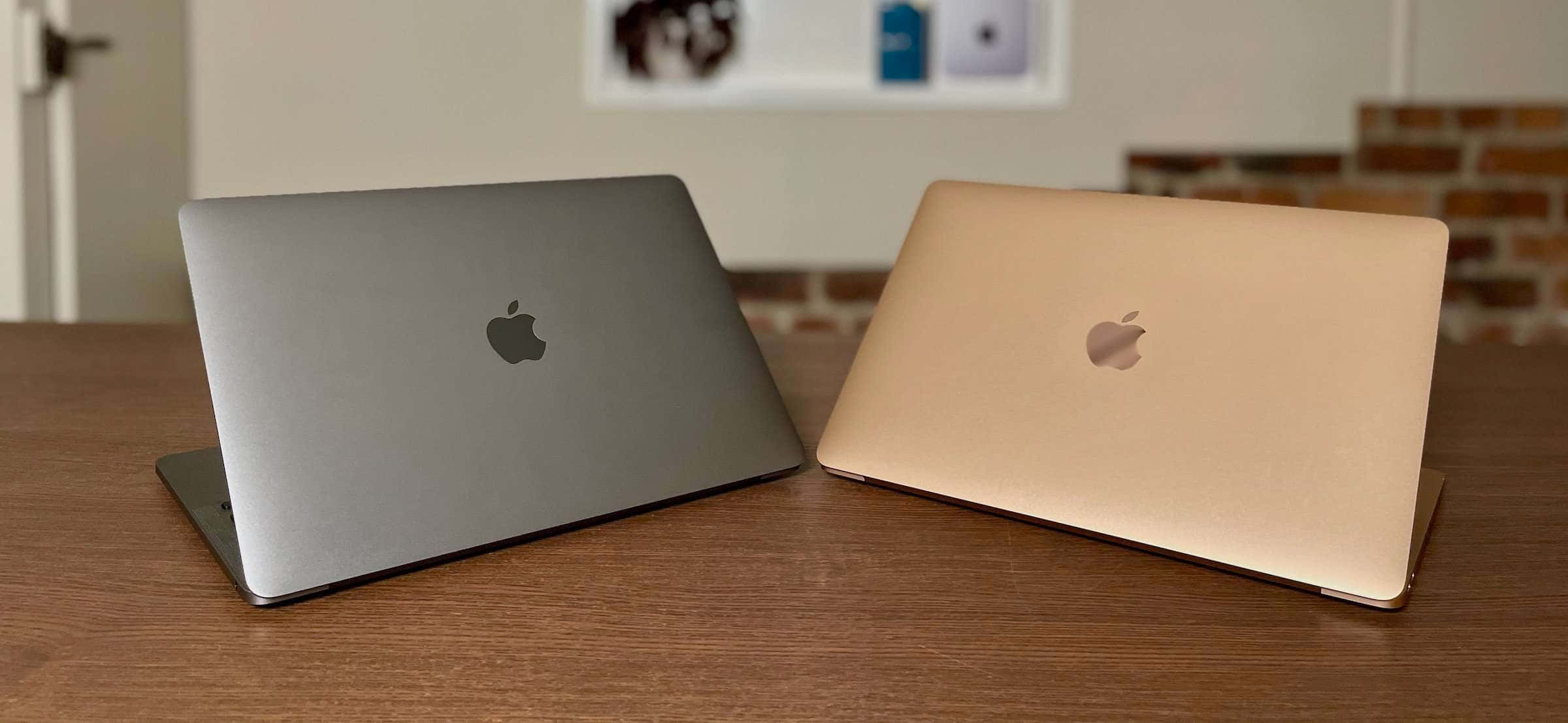 MacBook 動態圖片 桌布 壁紙 — 兩台 Apple 筆記型電腦銀色和金色闔上放在木桌上，背景有磚牆和裱框藝術品。