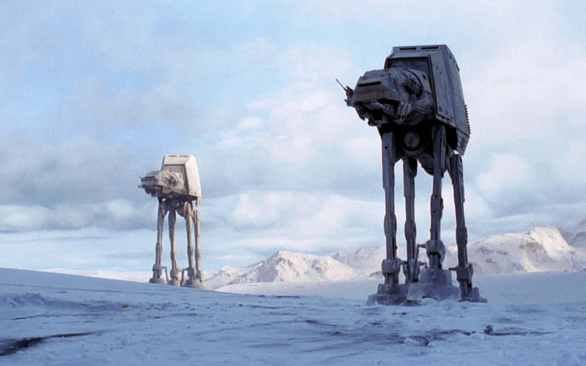 At-at 桌布 壁紙 — 兩台 AT-AT 步行機矗立在廣闊的雪地景觀中，遠方有山脈，天空多雲。