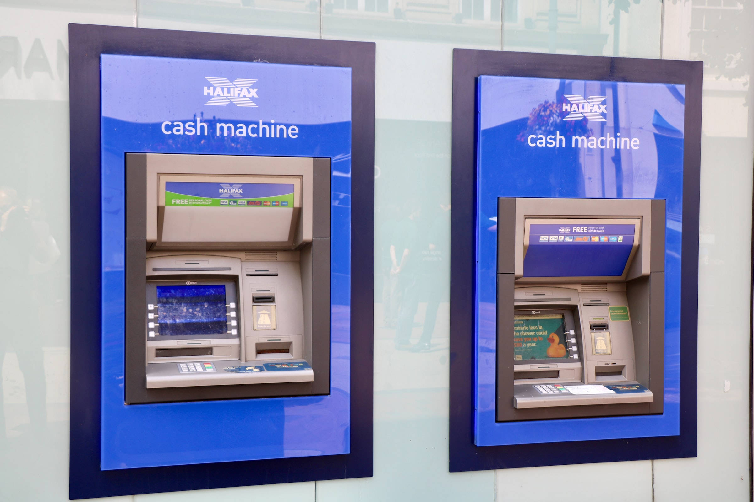 atm 桌布 壁紙 — 兩台 Halifax 提款機並排安裝在一個玻璃外牆、帶有藍色照明面板的小亭內。