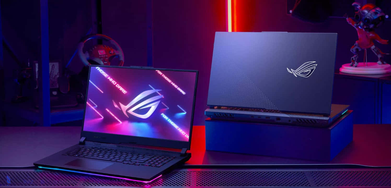 華碩 ROG 桌布 壁紙 — 兩台 ROG 電競筆電在黑暗的桌子上發出霓虹紫色和紅色的光芒，周圍環繞著電競裝備。