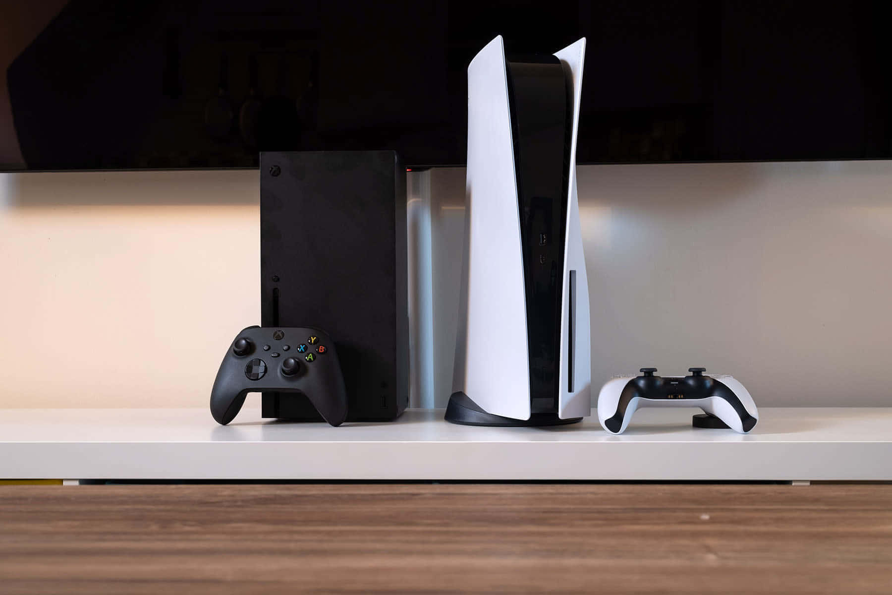 Xbox 桌布 壁紙 — 兩台現代遊戲主機和控制器並排放在乾淨的白色架子上，背景為深色。