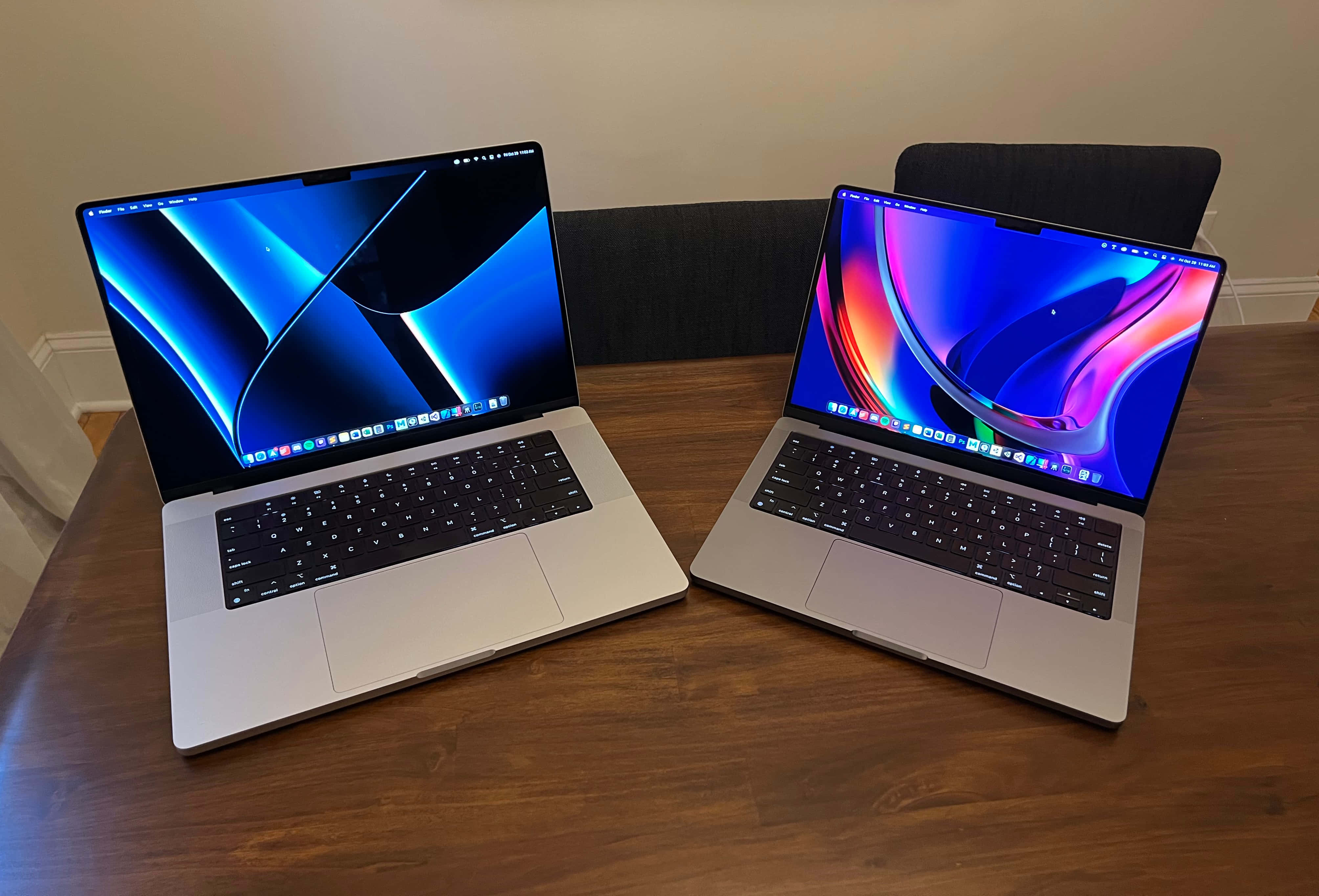 MacBook 動態圖片 桌布 壁紙 — 兩台銀色筆記型電腦展示充滿活力的抽象桌布，打開放在木桌上，房間光線柔和。