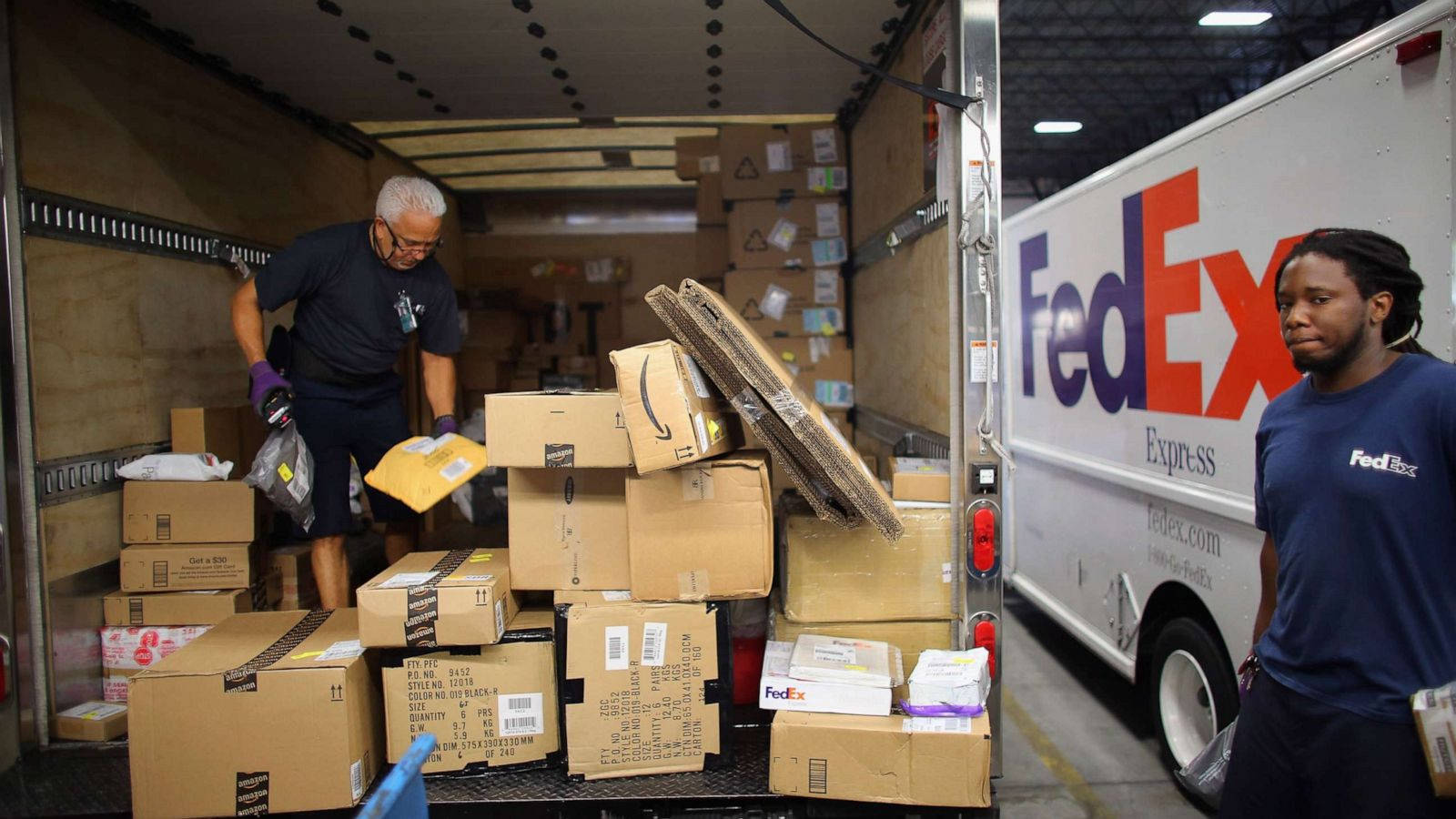 聯邦快遞 桌布 壁紙 — 兩名FedEx工人在倉庫環境中卸下一輛裝滿紙箱和包裹的貨車。