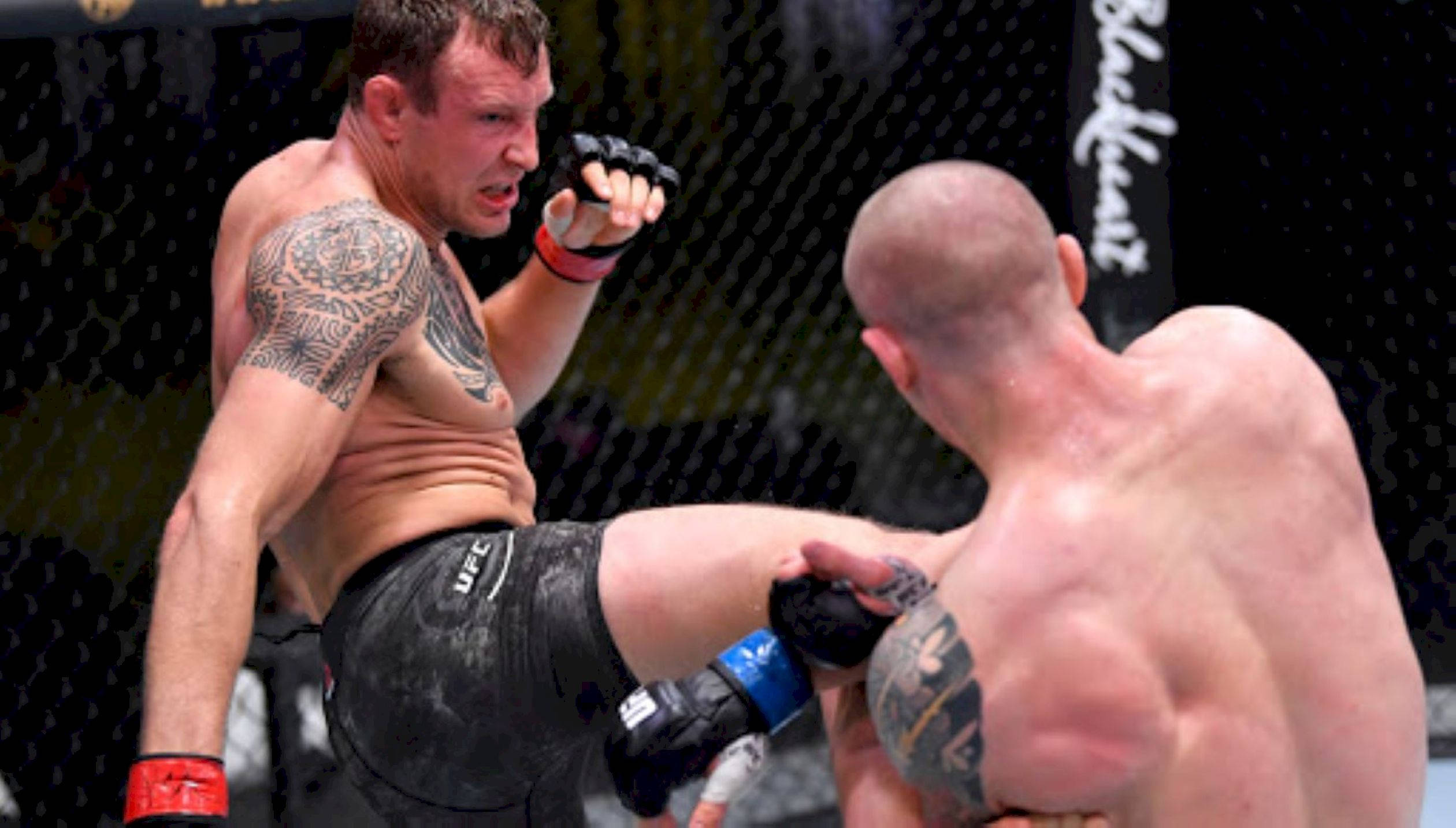 MMA 桌布 壁紙 — 兩名MMA拳手在八角籠中交鋒，一人使出高踢，另一人阻擋，汗水和紋身在明亮的場館燈光下閃閃發光。