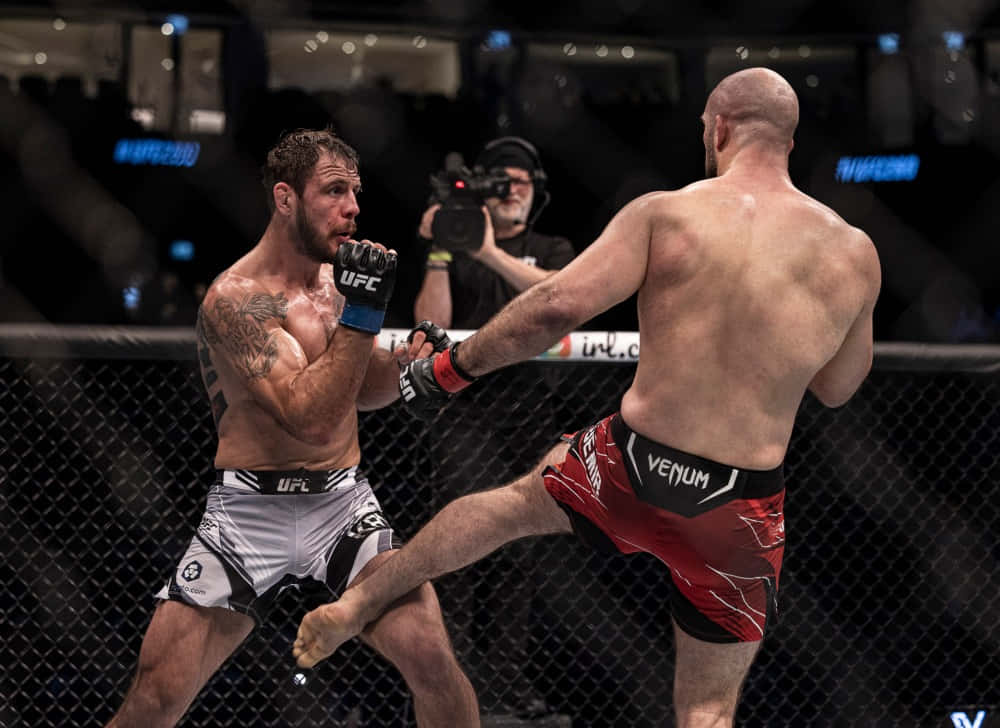 MMA 桌布 壁紙 — 兩名MMA拳手在八角籠中交鋒，一人使出高踢，另一人在緊張的籠鬥中阻擋。