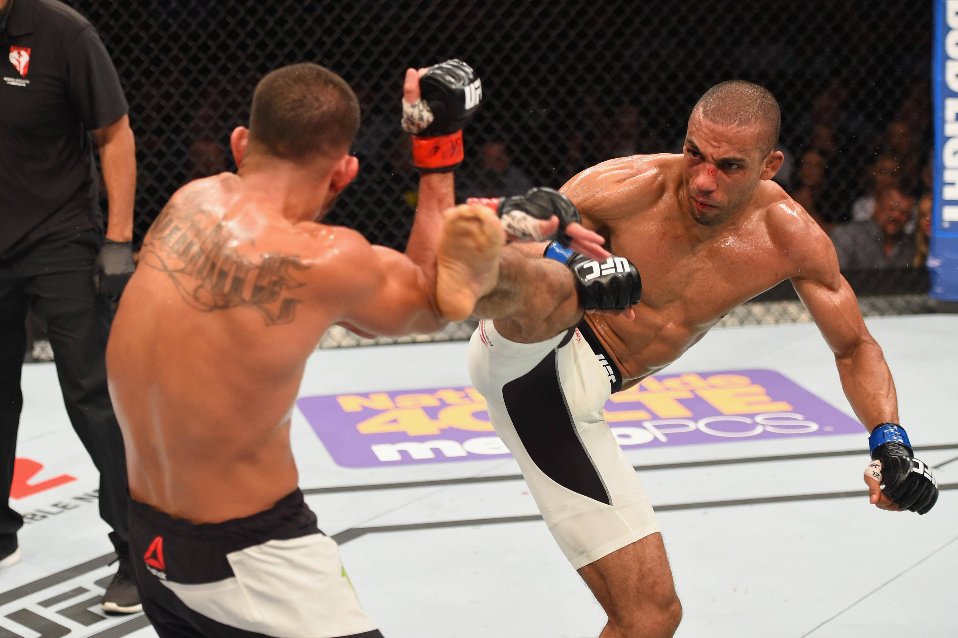 MMA 桌布 壁紙 — 兩名MMA拳手在八角籠中交鋒，一人使出高踢，另一人阻擋，汗水在她們肌肉發達的身體上閃閃發光。