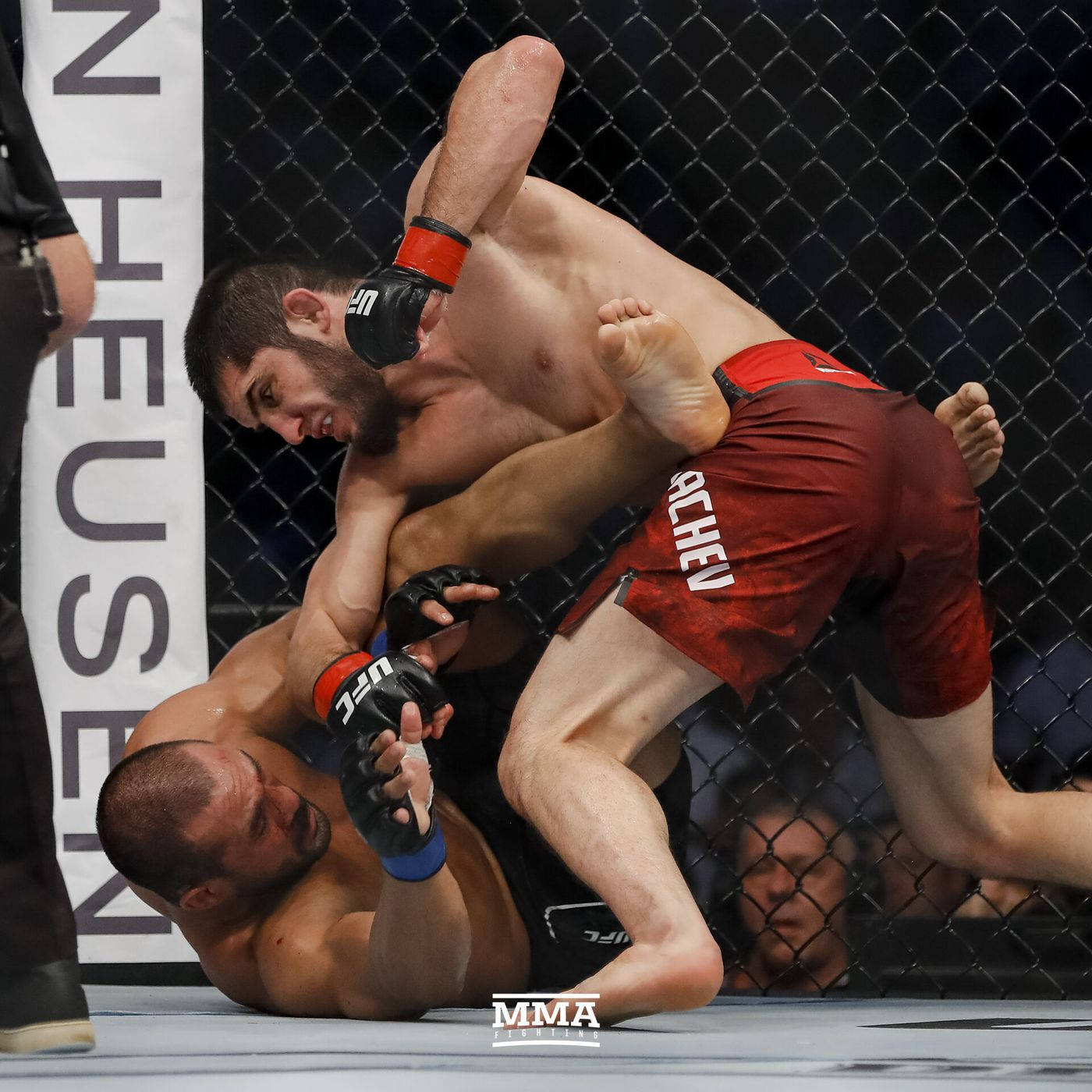 Islam Makhachev 桌布 壁紙 — 兩名MMA拳手在八角籠內激烈纏鬥，其中一人對對手施展腿鎖。