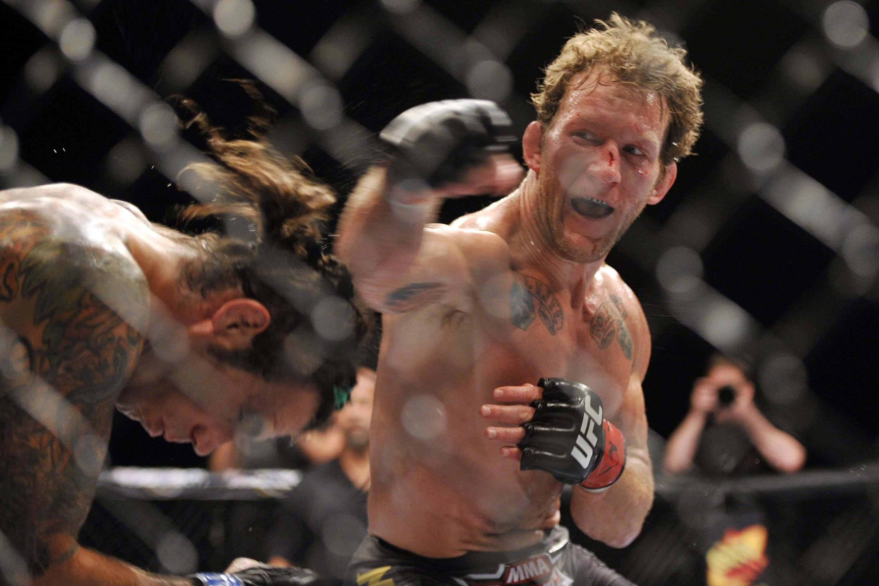 Fight 桌布 壁紙 — 兩名MMA拳手在激烈的鐵籠比賽中，汗水飛濺，其中一名拳手打出強力一拳。