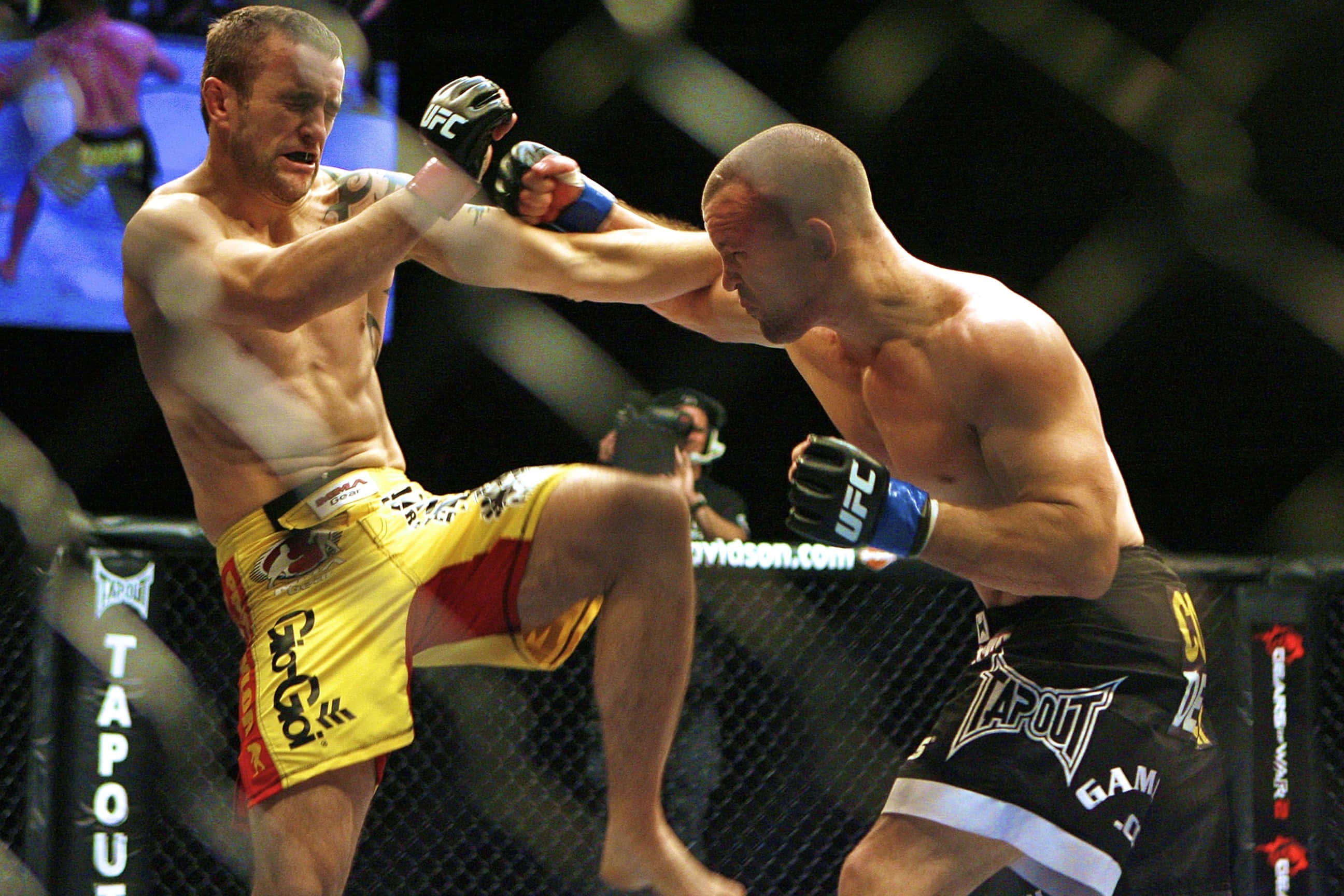 UFC 桌布 壁紙 — 兩名MMA拳手在激烈的鐵籠賽中交鋒，其中一人使出高踢，另一人則阻擋。