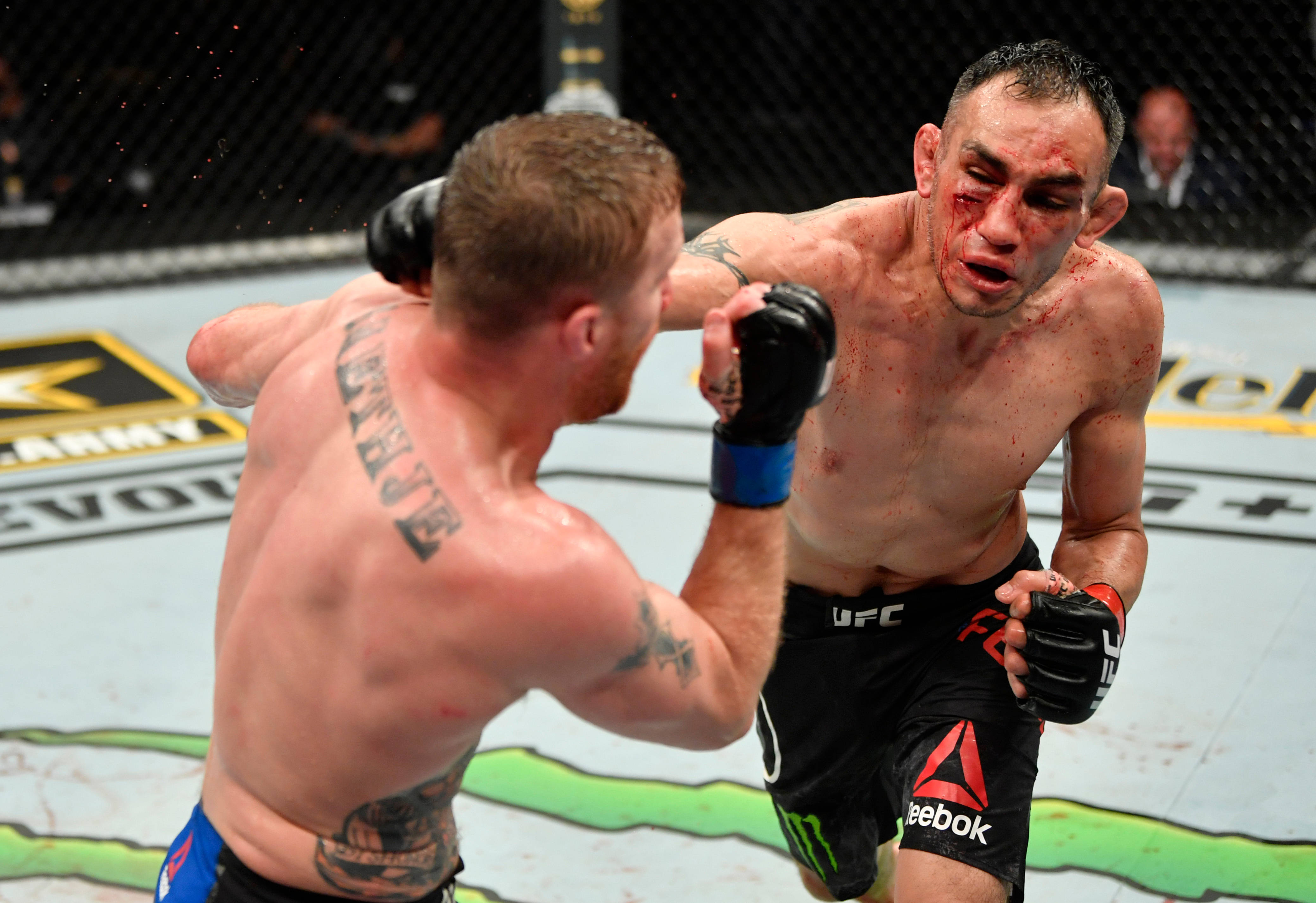 UFC 桌布 壁紙 — 兩名MMA拳手在激烈的鐵籠賽中交鋒，在明亮的場館燈光下可見血跡斑斑的臉龐和刺青。