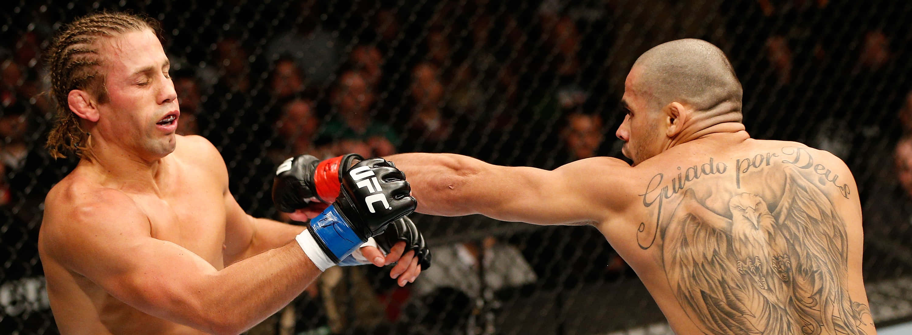 UFC 桌布 壁紙 — 兩名MMA拳手在激烈的鐵籠賽中交鋒，一人打出強力一拳，另一人以手套和可見的刺青進行阻擋。