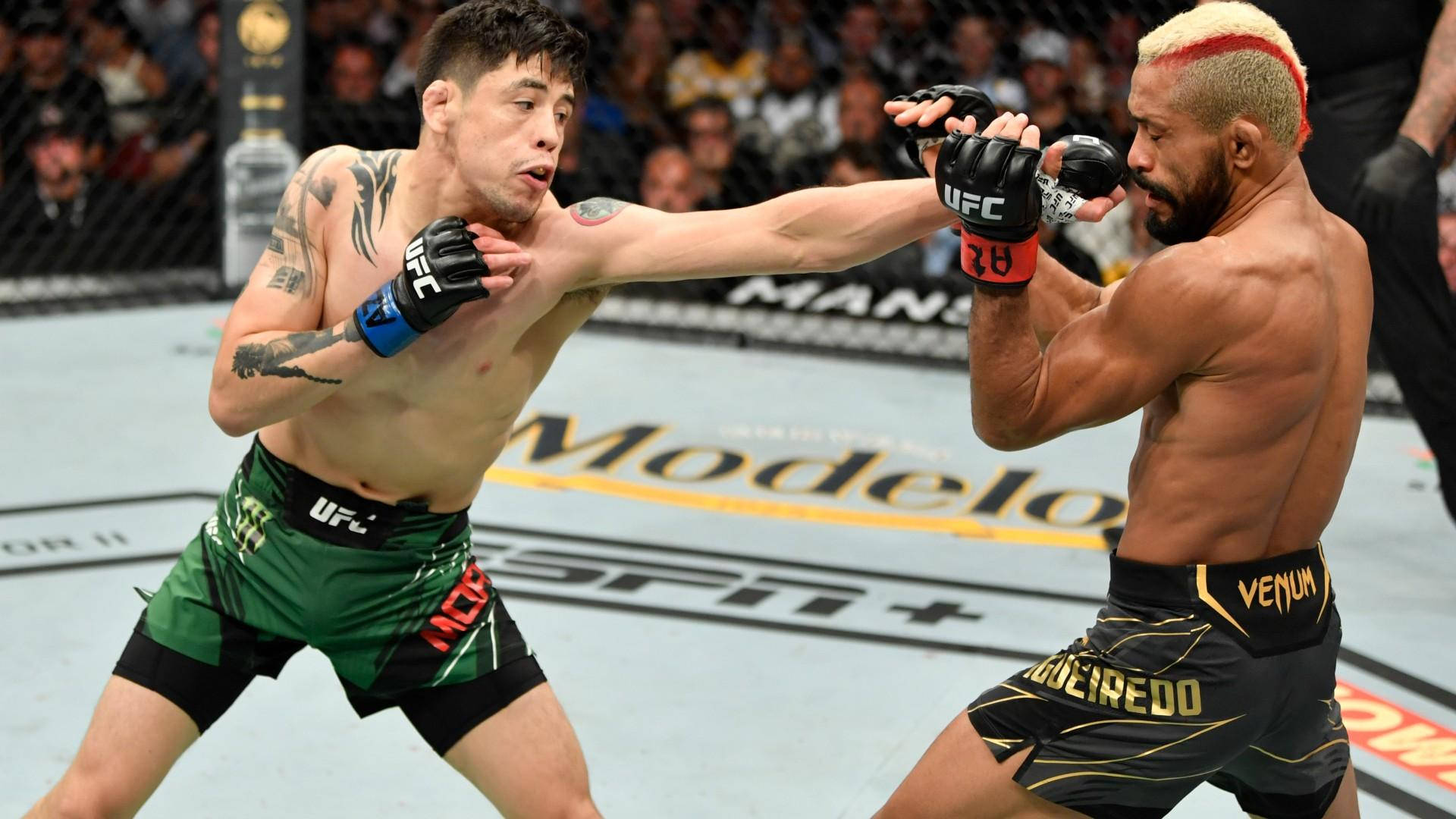 Brandon Moreno 桌布 壁紙 — 兩名MMA拳手在激烈的鐵籠賽中交鋒，一人打出強力一拳，另一人則進行阻擋。