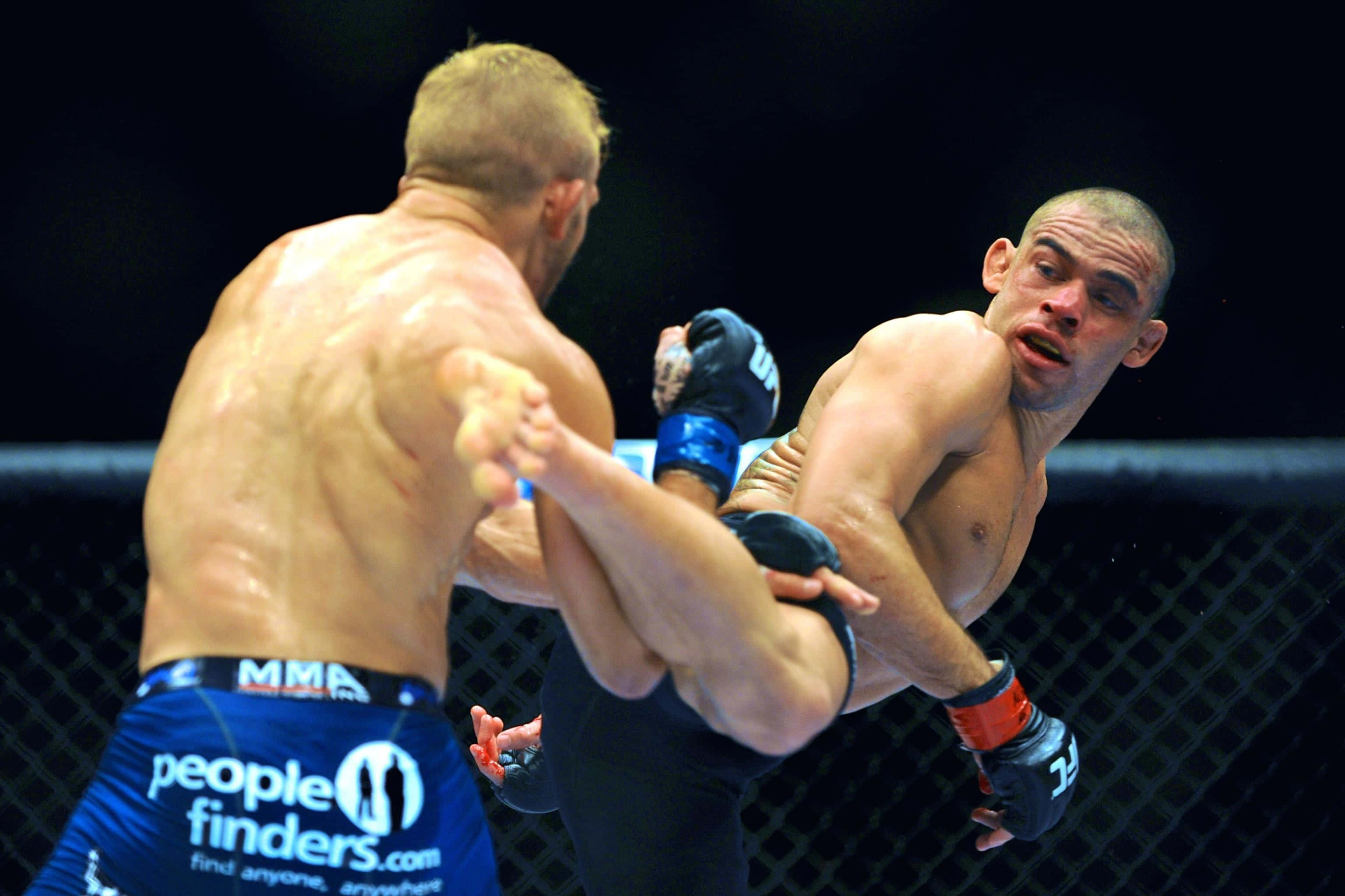 UFC 桌布 壁紙 — 兩名MMA拳手在籠中交鋒，一人使出強力踢擊，另一人則在汗流浹背的激烈時刻阻擋。