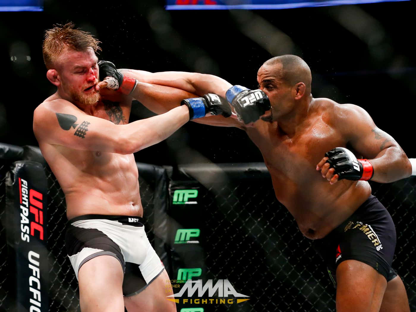 UFC 桌布 壁紙 — 兩名MMA拳手在籠中交鋒，其中一人打出強力一拳，汗水在明亮的場館燈光下飛濺。
