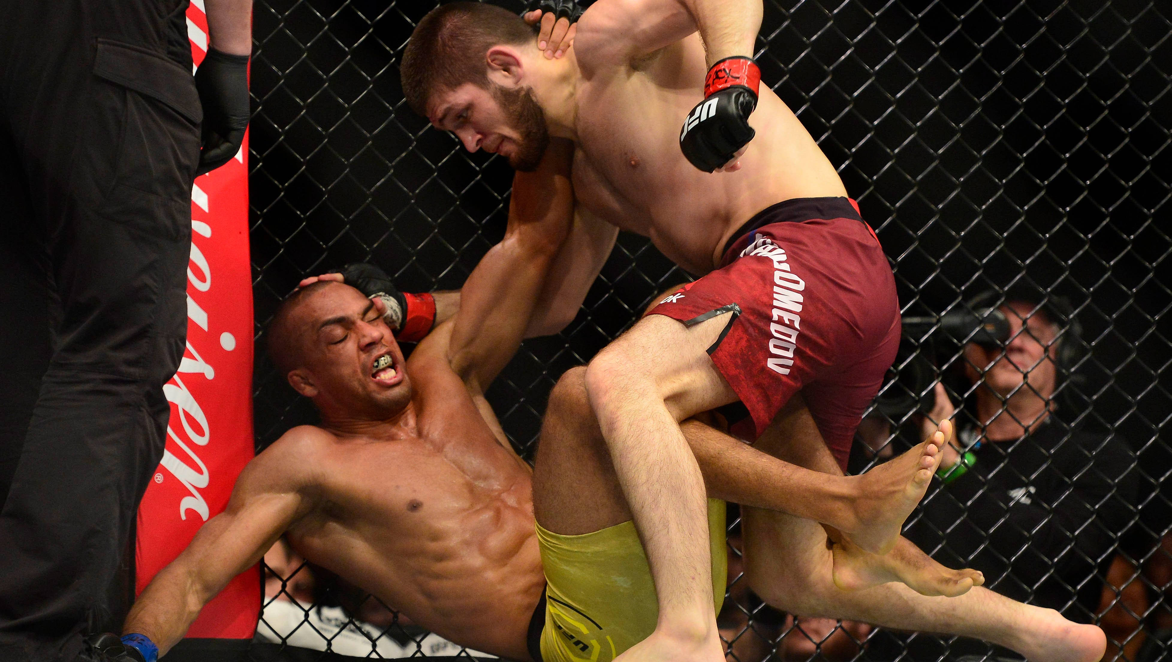 MMA 桌布 壁紙 — 兩名MMA拳手在籠式八角籠內激烈纏鬥，其中一人正在施展降服技。