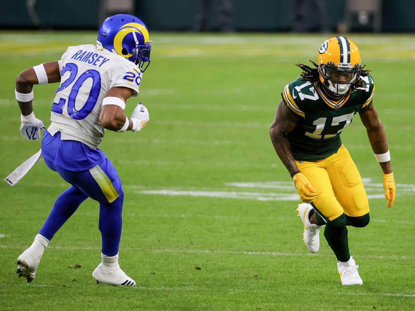 足球 桌布 壁紙 — 兩名NFL球員在充滿活力的綠色場地上行動，一人身穿藍色和金色制服，另一人身穿綠色和黃色制服，兩人都全力衝刺。