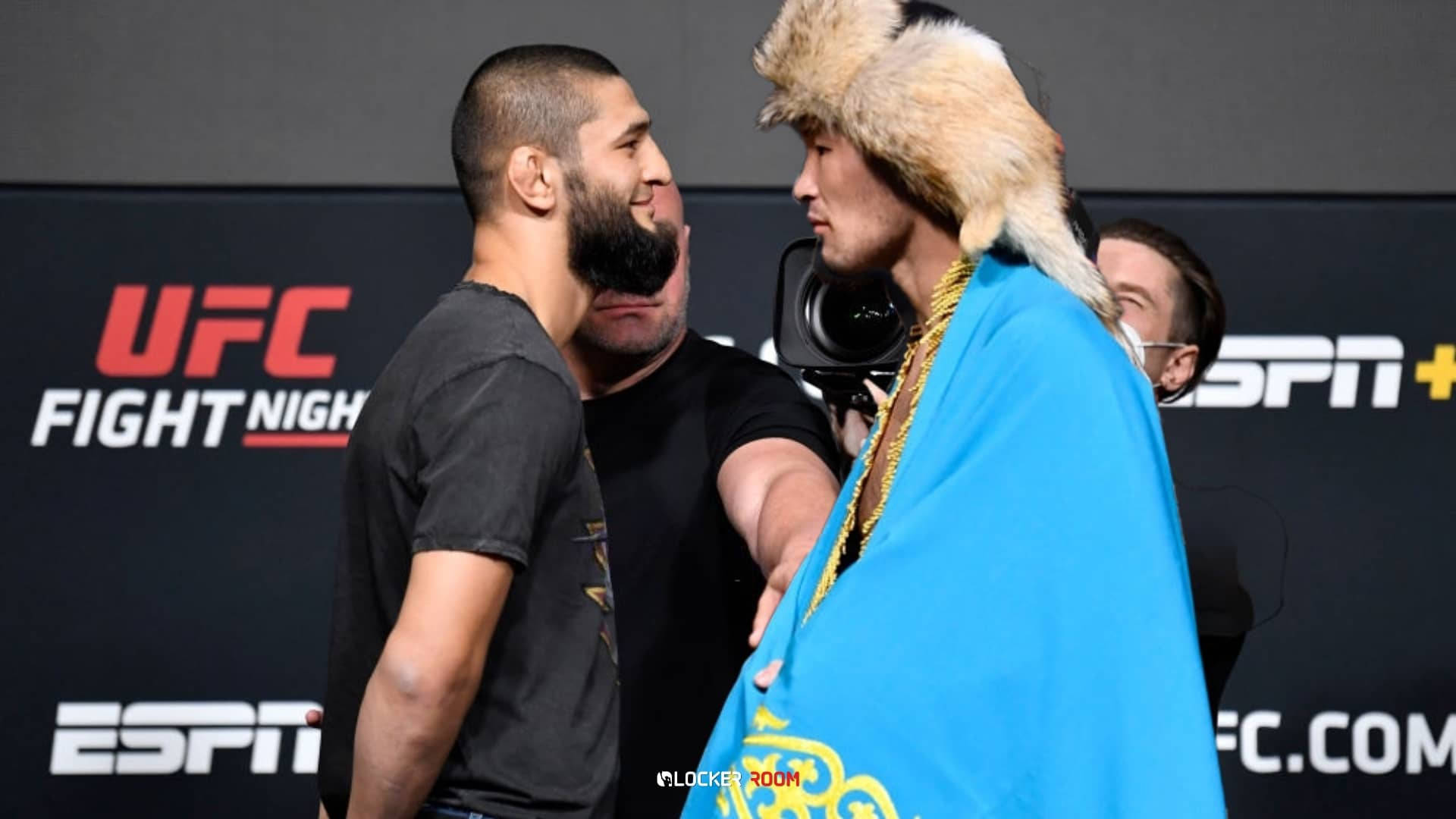 UFC 桌布 壁紙 — 兩名UFC拳手在稱重時對峙，一人戴皮帽和藍色國旗，另一人穿黑色T恤，兩人都專注而緊張。