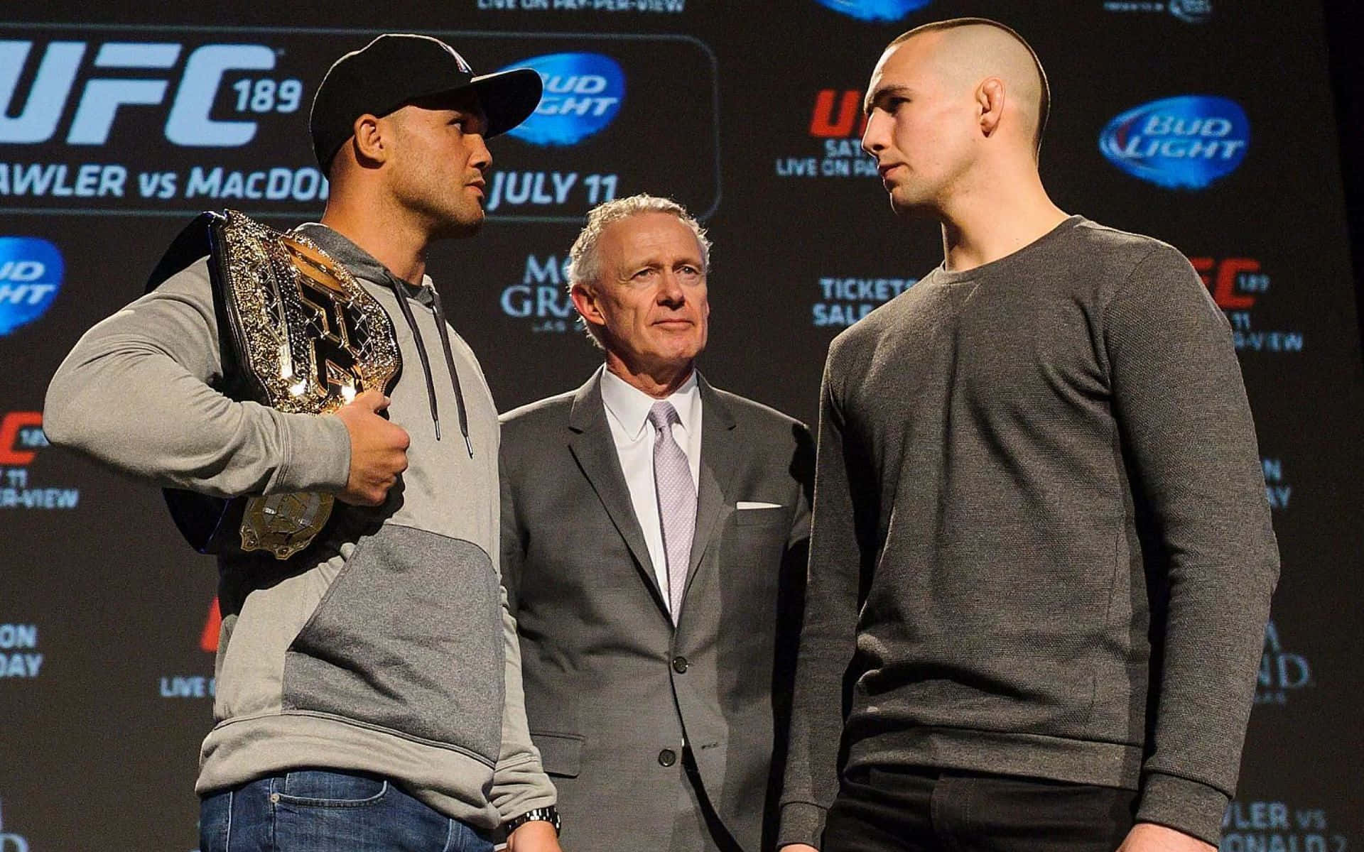 Champion 桌布 壁紙 — 兩名UFC拳手在稱重活動中對峙，裁判站在他們之間，冠軍腰帶展示在旁。