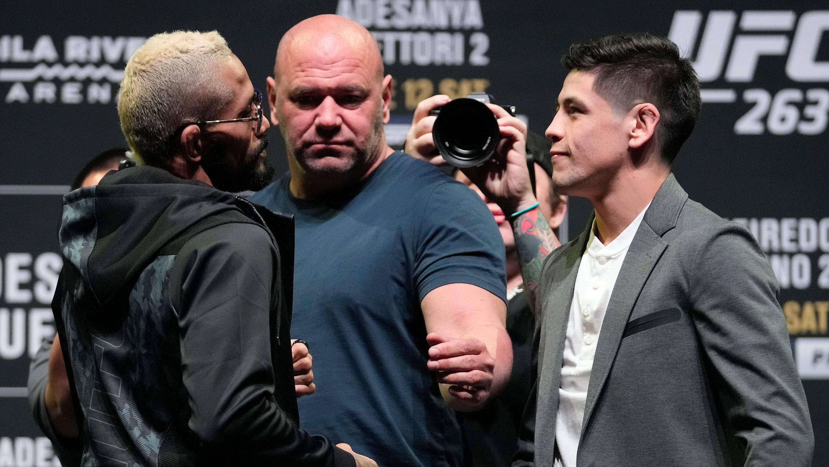 UFC 桌布 壁紙 — 兩名UFC拳手在記者會上對峙，中間有裁判，攝影師捕捉緊張時刻。
