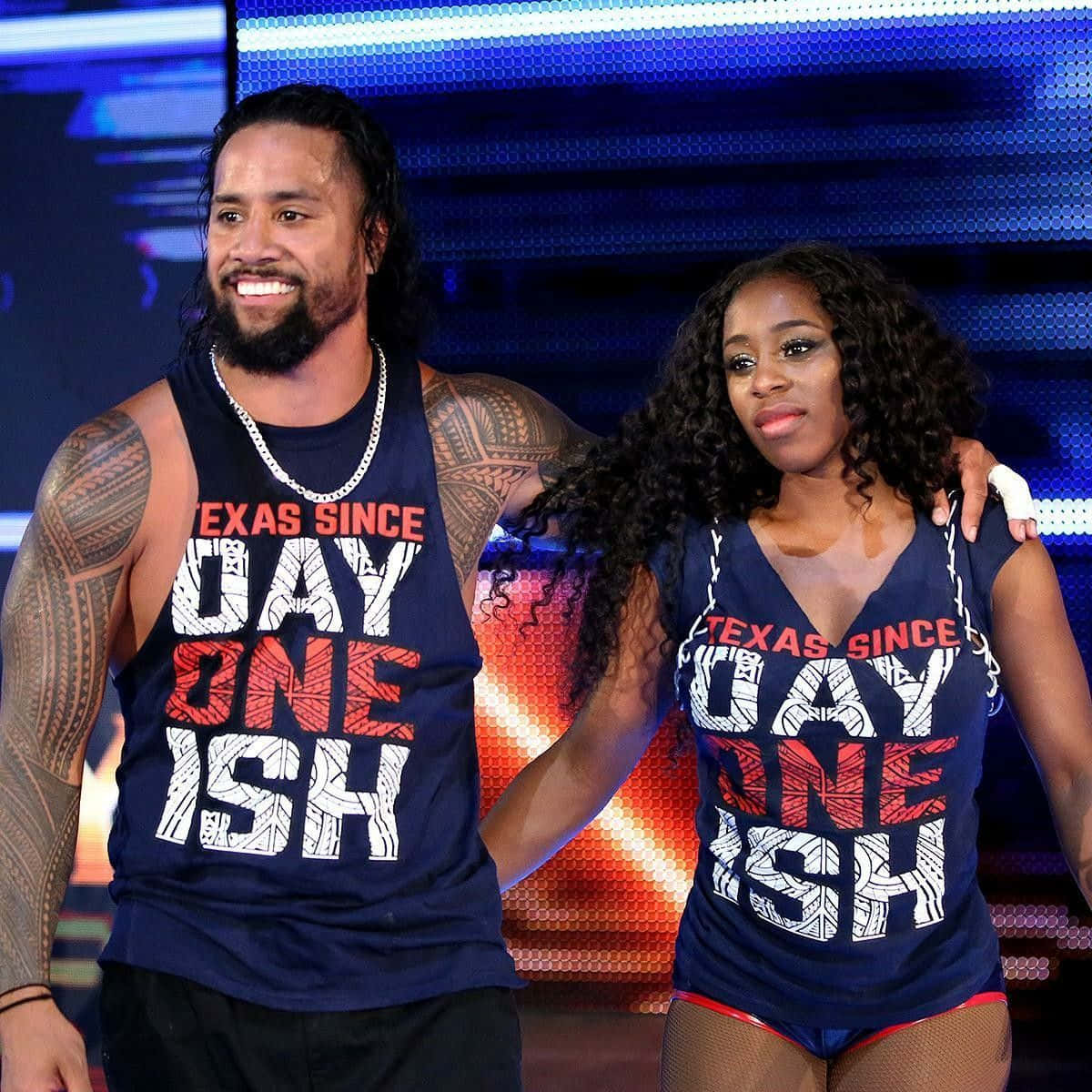 Team 桌布 壁紙 — 兩名WWE摔角手穿著相配的「Texas Since Day One Ish」背心，在充滿活力的藍色和橙色數位背景前自信地擺姿勢。